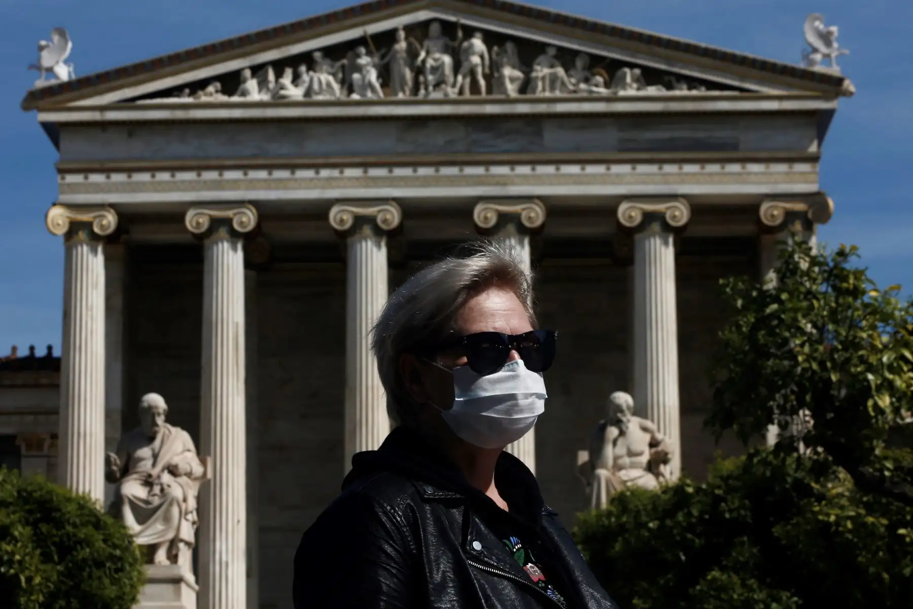 Una mujer con una máscara espera un autobús mientras se para frente al edificio de la Academia de Atenas, en Grecia. Foto: EFE