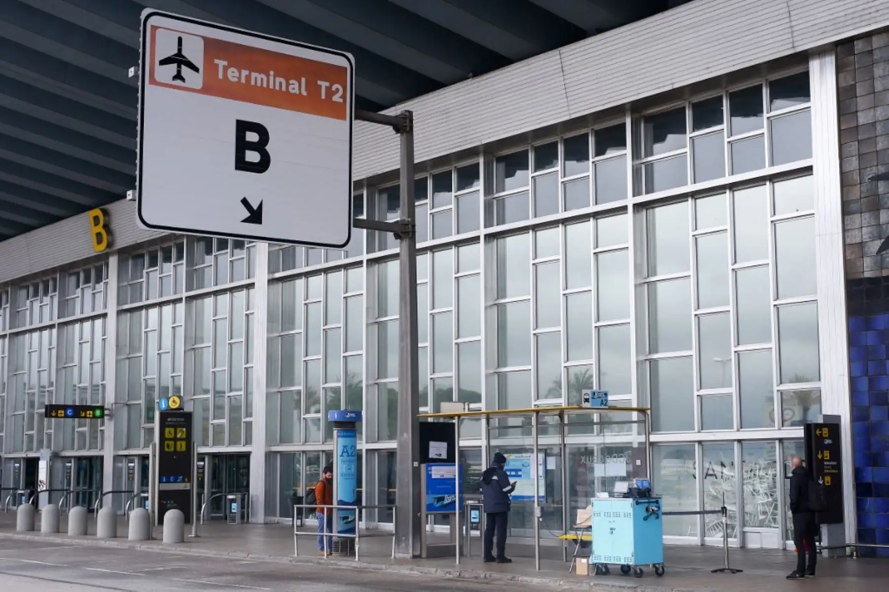Tres personas esperan el autobús en la Terminal 2 del aeropuerto de Barcelona. Foto: AFP