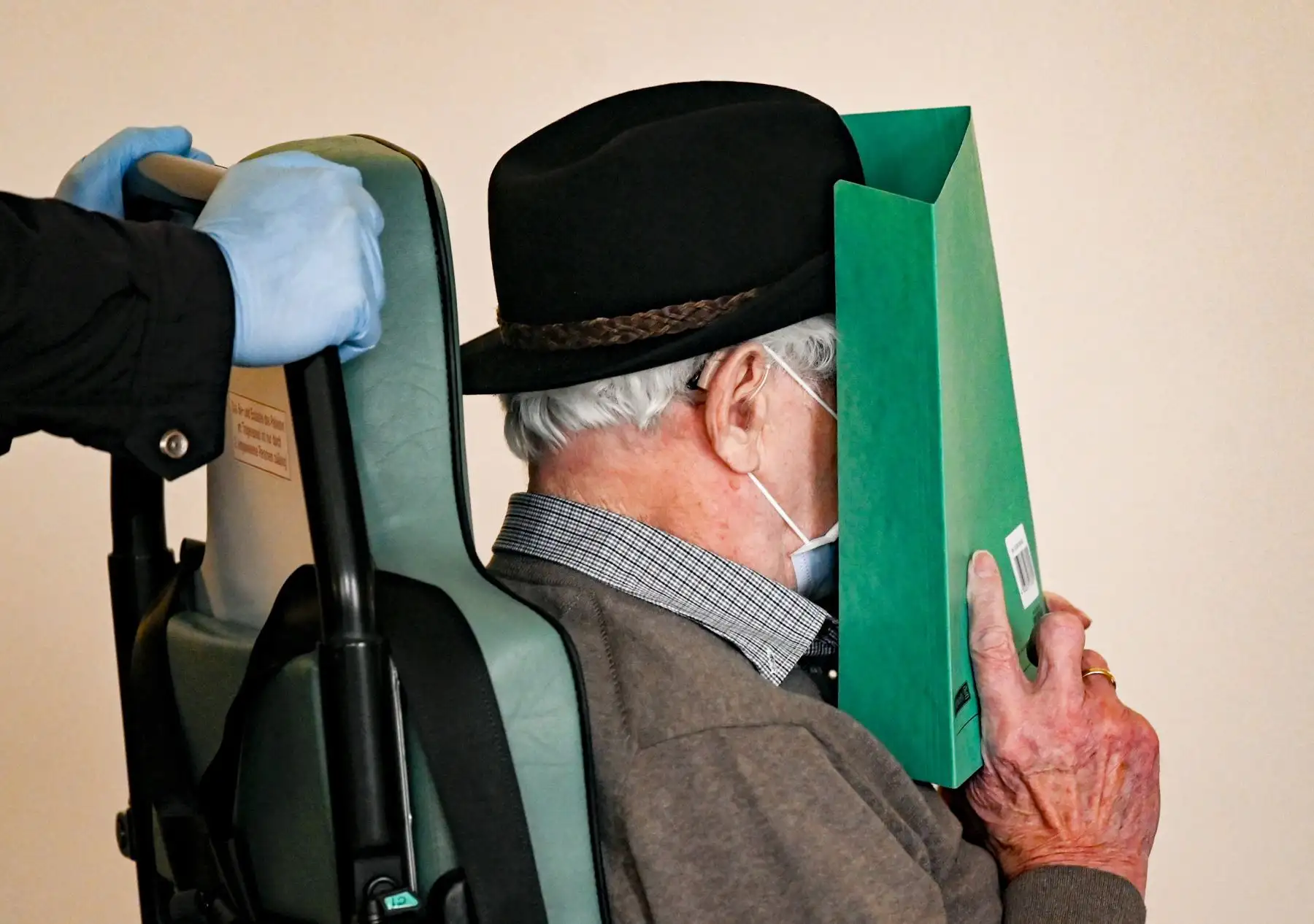 Bruno Dey, un ex vigilante de las SS en el campo de concentración de Stutthof, se cubre la cara cuando lo llevan en una silla de ruedas a la sala del tribunal para una audiencia en su juicio el 20 de marzo. Coronavirus COVID-19. Foto: AFP