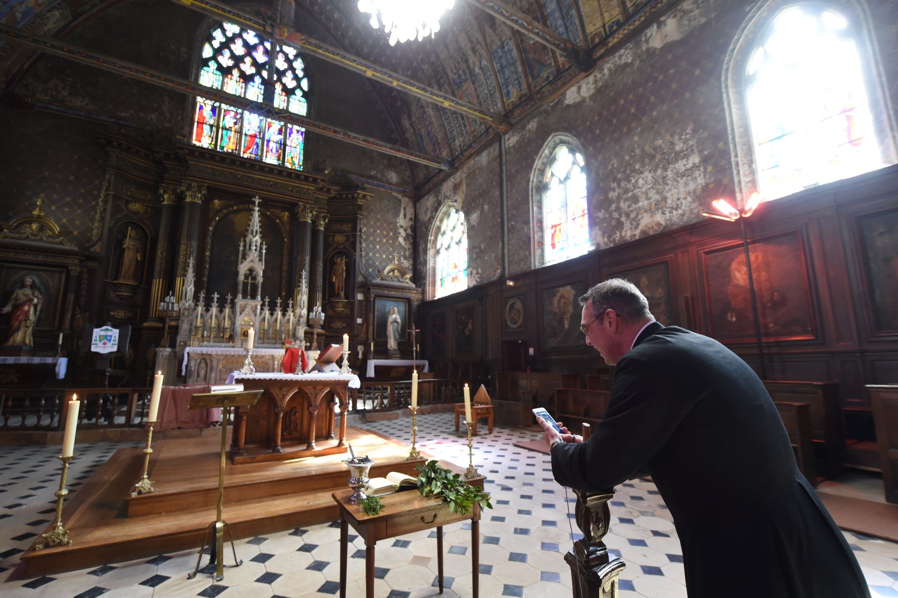 Un sacerdote francés transmite una misa del Domingo de Ramos con una aplicación de video chat en su teléfono inteligente fijada en un candelabro de madera frente al altar. Foto: AFP