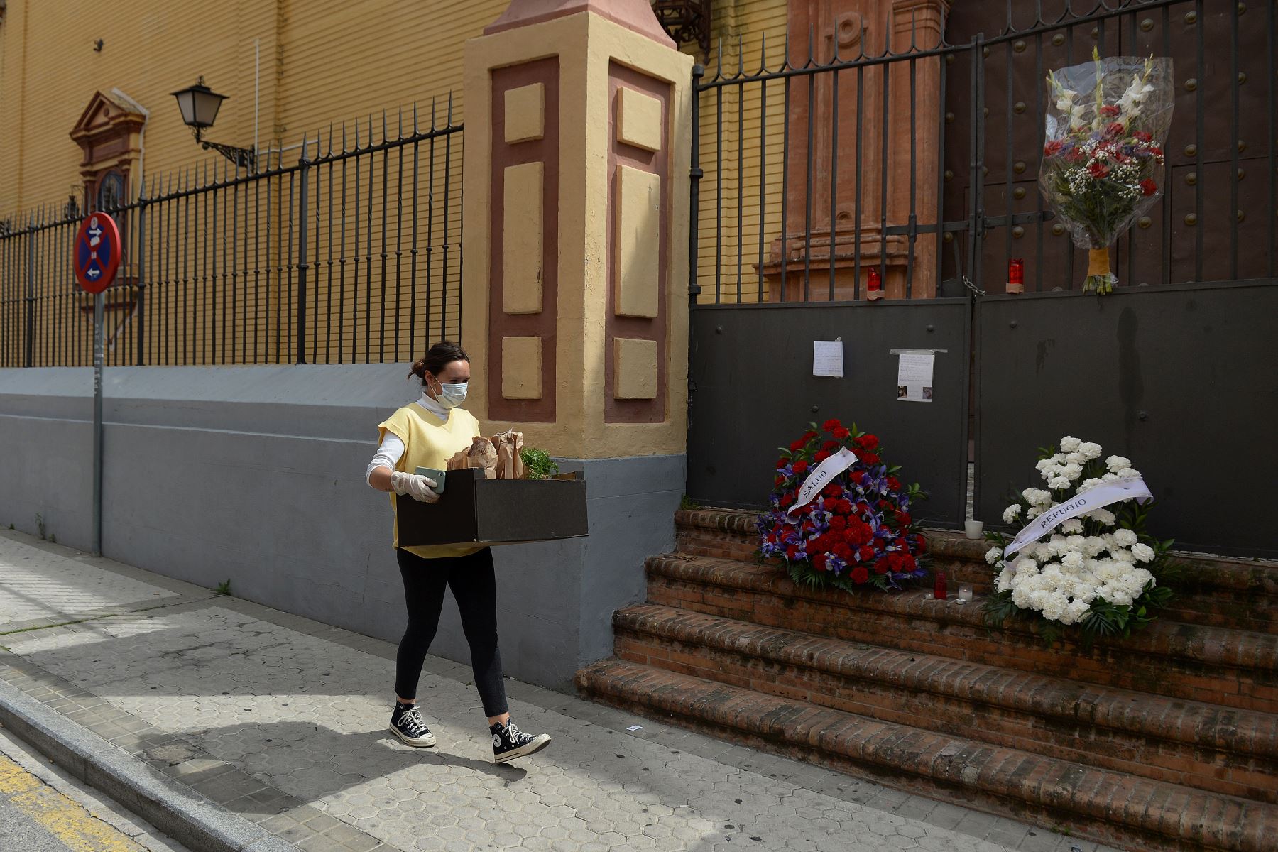 Una mujer lleva una caja con comida, pasa junto a la iglesia de San Bernardo en Sevilla, adornada con flores dejadas por los fieles cuando las procesiones de Pascua fueron canceladas para evitar la propagación del coronavirus,
Foto:AFP