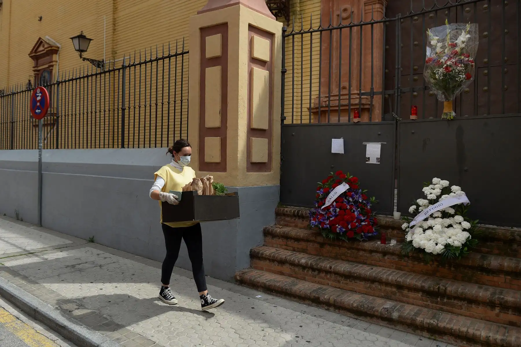 Una mujer lleva una caja con comida, pasa junto a la iglesia de San Bernardo en Sevilla, adornada con flores dejadas por los fieles cuando las procesiones de Pascua fueron canceladas para evitar la propagación del coronavirus,
Foto:AFP