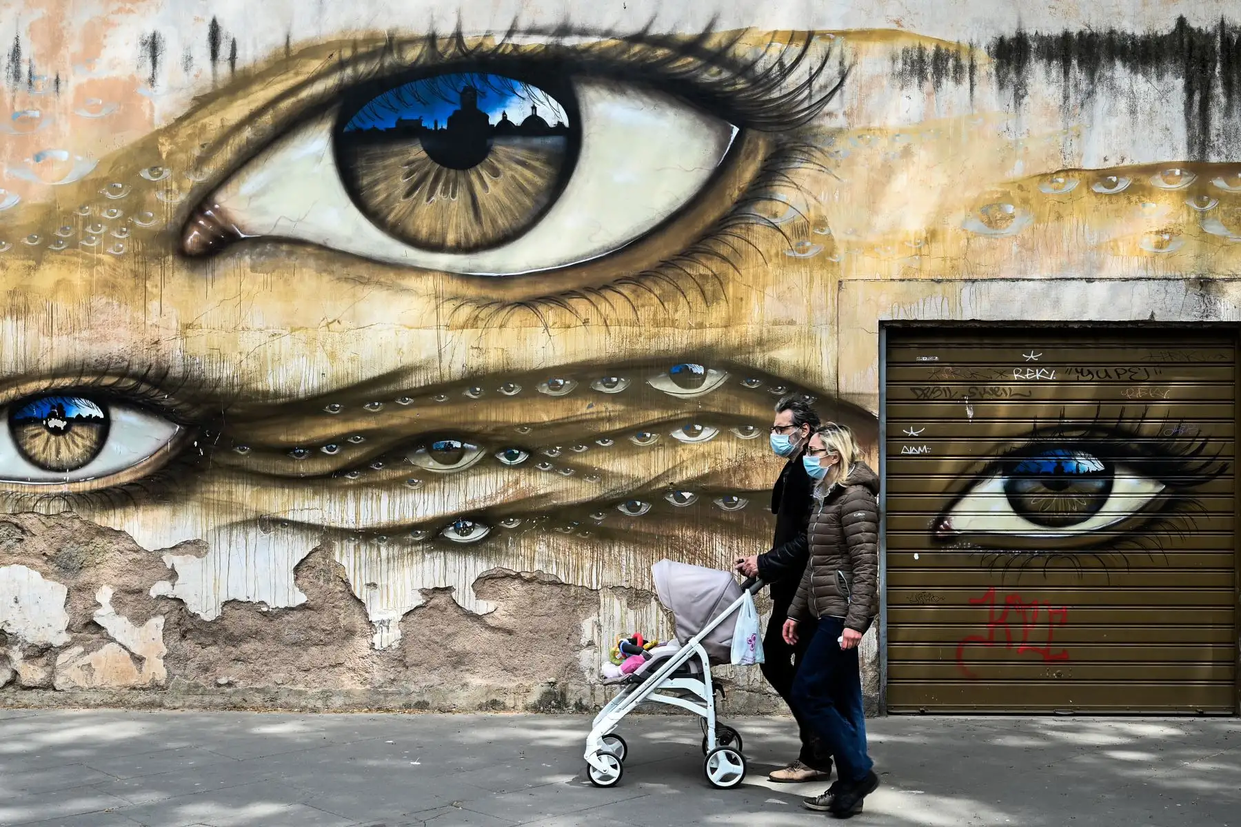 Una pareja con máscaras faciales y empujando un cochecito pasa junto a un mural en el distrito Trastevere de Roma  durante el cierre del país destinado a frenar la propagación de la infección por COVID-19, causada por el nuevo coronavirus. AFP
