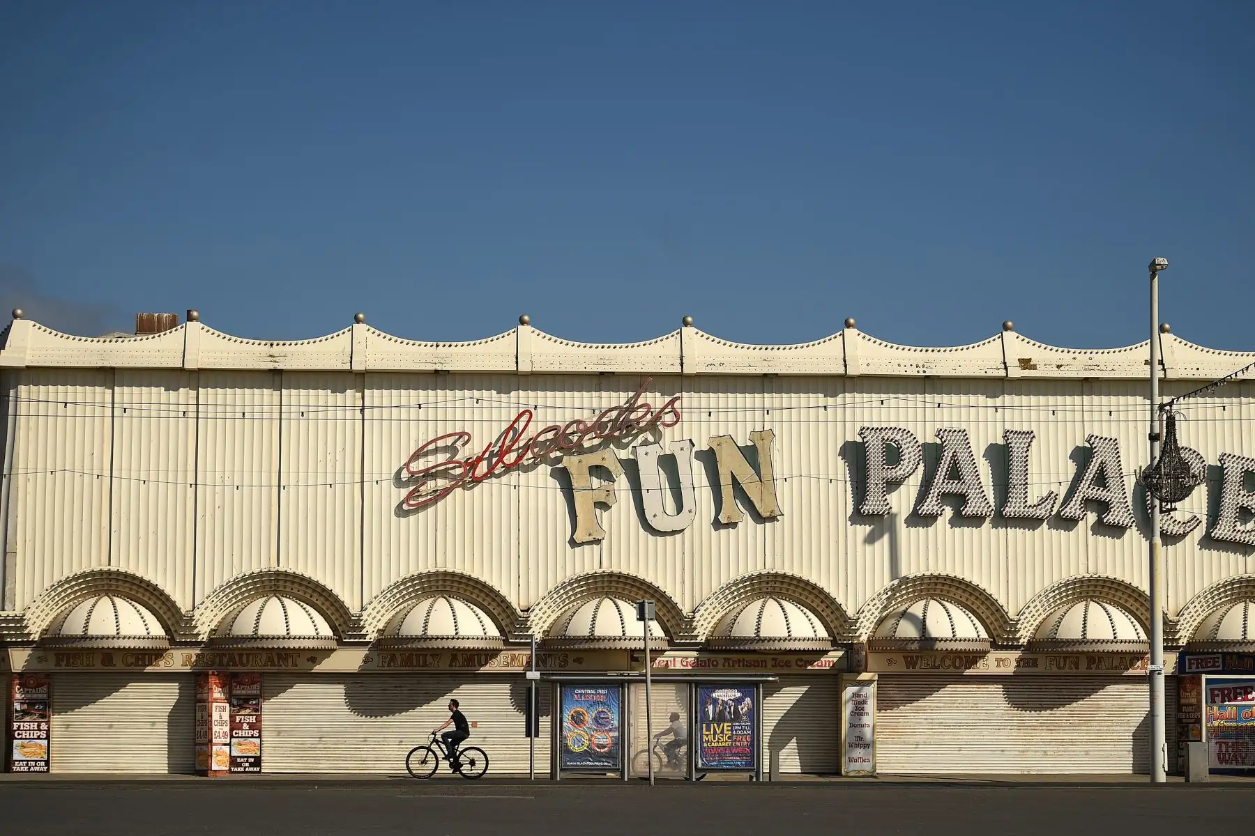 Las personas andan en bicicleta frente a una sala de juegos, cerrada debido a las restricciones de COVID-19, en el paseo marítimo bajo el sol de primavera en la costa de Blackpool, en el noroeste de Inglaterra. AFP