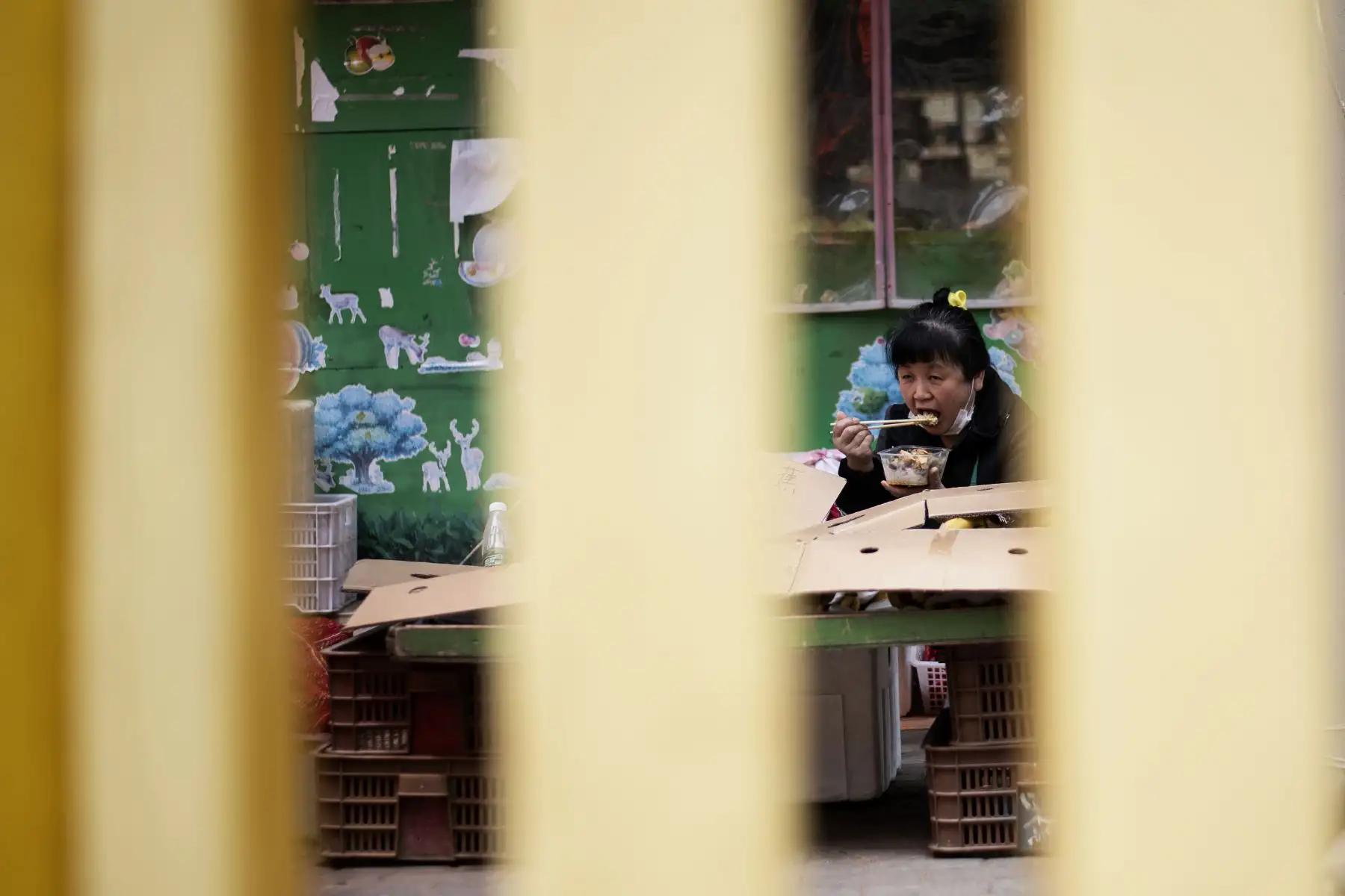 Un vendedor con su mascarilla hacia abajo come dentro de un complejo residencial barricado en Wuhan.
Foto: AFP