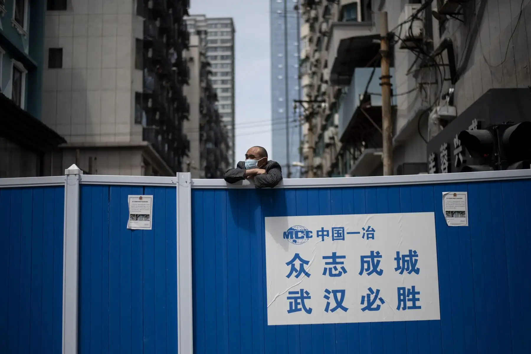 Un hombre con una máscara facial mira sobre una barricada creada para mantener a las personas fuera de un complejo residencial en Wuhan.
Foto: AFP
