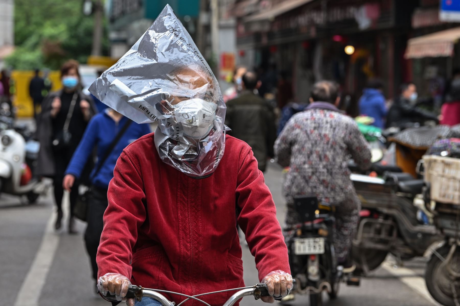 Un hombre con una máscara facial y una bolsa de plástico en la cabeza monta una bicicleta en una calle de Wuhan. Foto: AFP