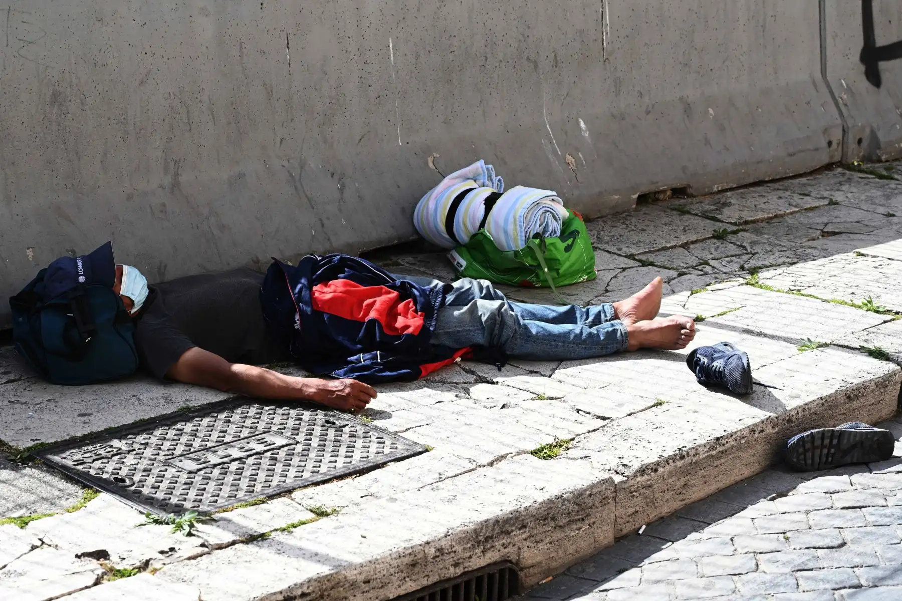 Una persona sin hogar que usa una máscara protectora yace dormida en el pavimento en la Piazza Venezia central de Roma el 17 de abril de 2020 durante un encierro destinado a frenar la propagación de la infección COVID-19, causada por el nuevo coronavirus. Foto: AFP