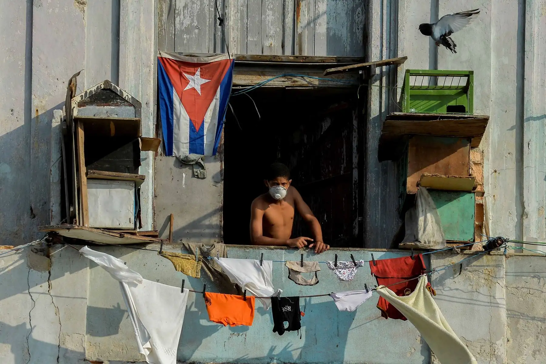 Un hombre se asoma desde su balcón usando una máscara protectora contra el COVID-19. La isla comunista de un solo partido está teniendo dificultades para obtener suministros médicos. Foto: AFP