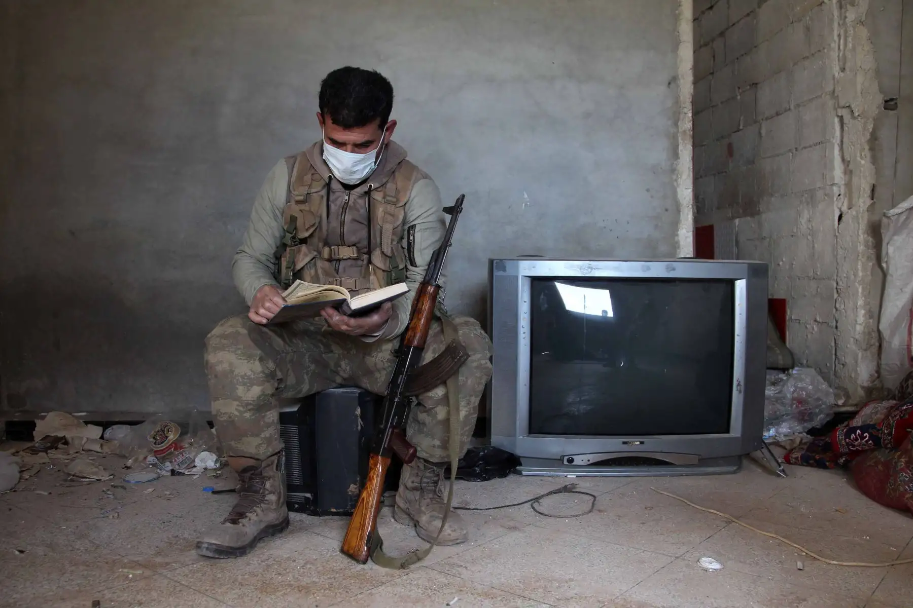 Un luchador sirio respaldado por Turquía con una máscara facial hojea un libro mientras descansa en una posición en el pueblo de Aafes, al norte de la ciudad de Saraqib, en la provincia noroccidental de Idlib, durante la nueva crisis pandémica de coronavirus. Foto: AFP