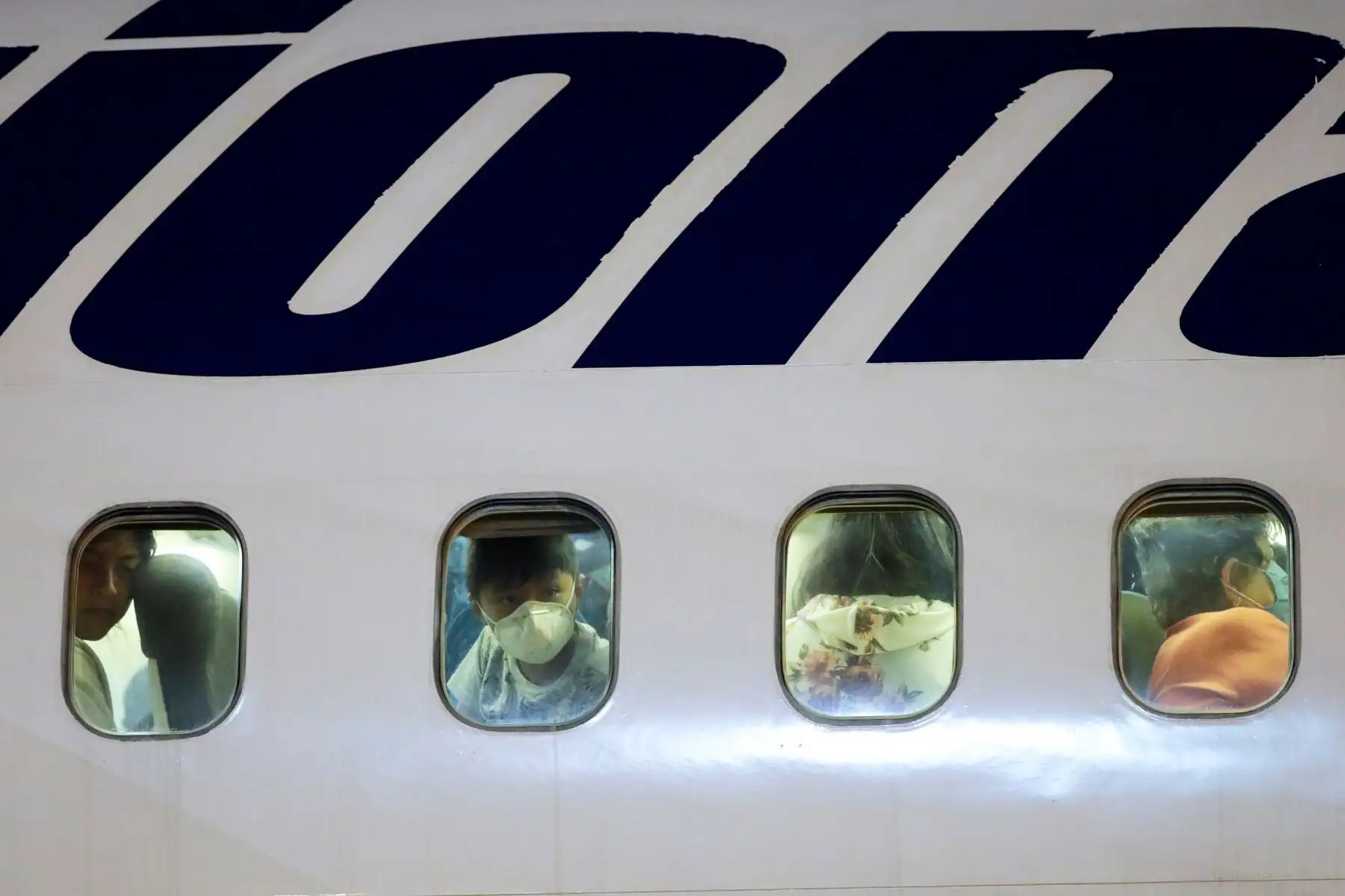 Algunos de los 123 ecuatorianos que se habían quedado varados en México en medio de la crisis por la pandemia observan a miembros de la Cruz Roja Internacional estibar insumos médicos en el avión que los trasladará a Ecuador, en el Aeropuerto Internacional Panamá Pacífico, en Ciudad de Panamá (Panamá). Foto: EFE