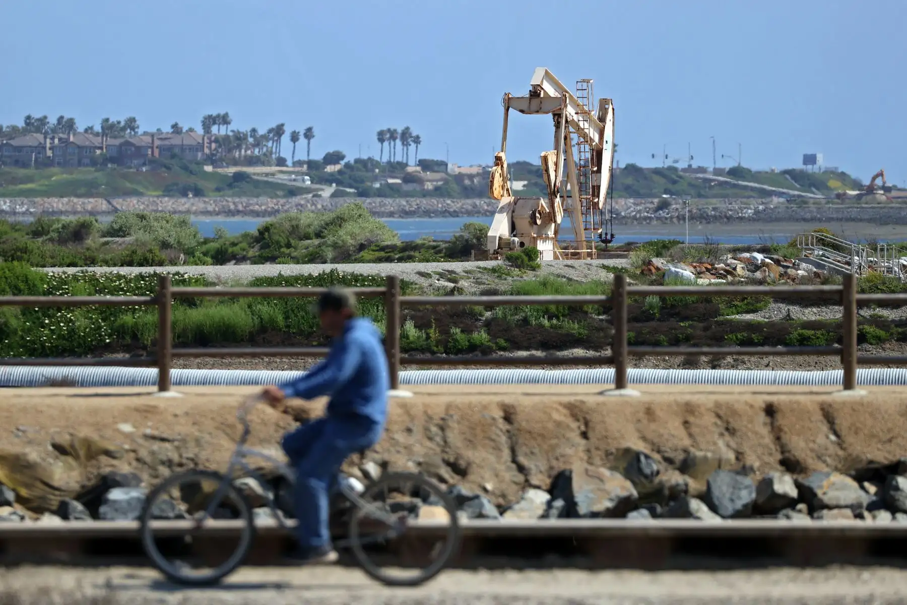 Una persona monta una bicicleta en un camino frente a una torre de perforación de petróleo cerca de los campos petrolíferos de Huntington Beach, California. Foto: AFP