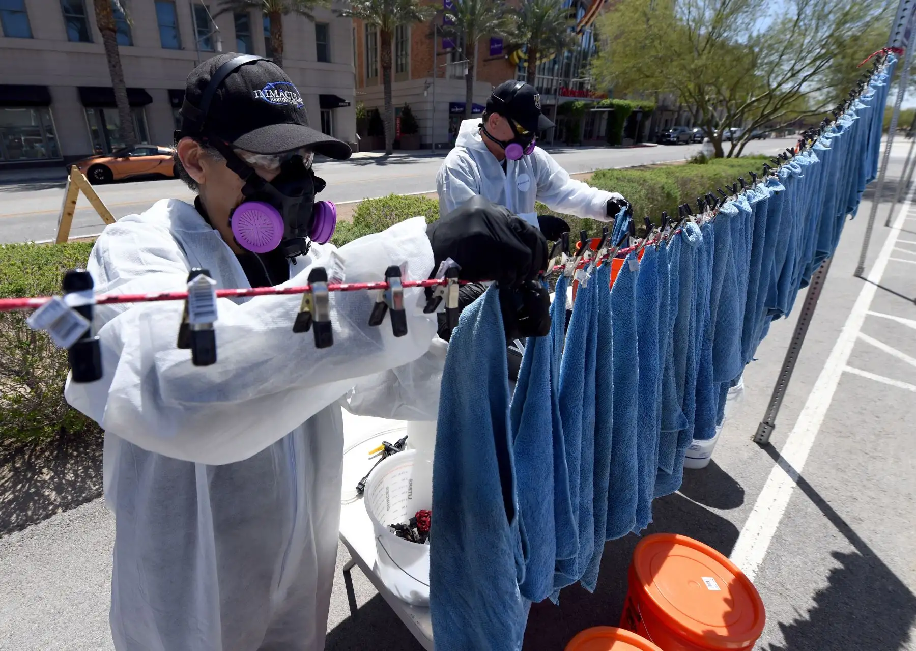 Yolanda Hernández (L) y Adam Gunn de Immaculate Restoration & Carpet Care desinfectan los paños de microfibra utilizados para limpiar vehículos en medio de la pandemia de coronavirus en el estacionamiento del Discovery Children