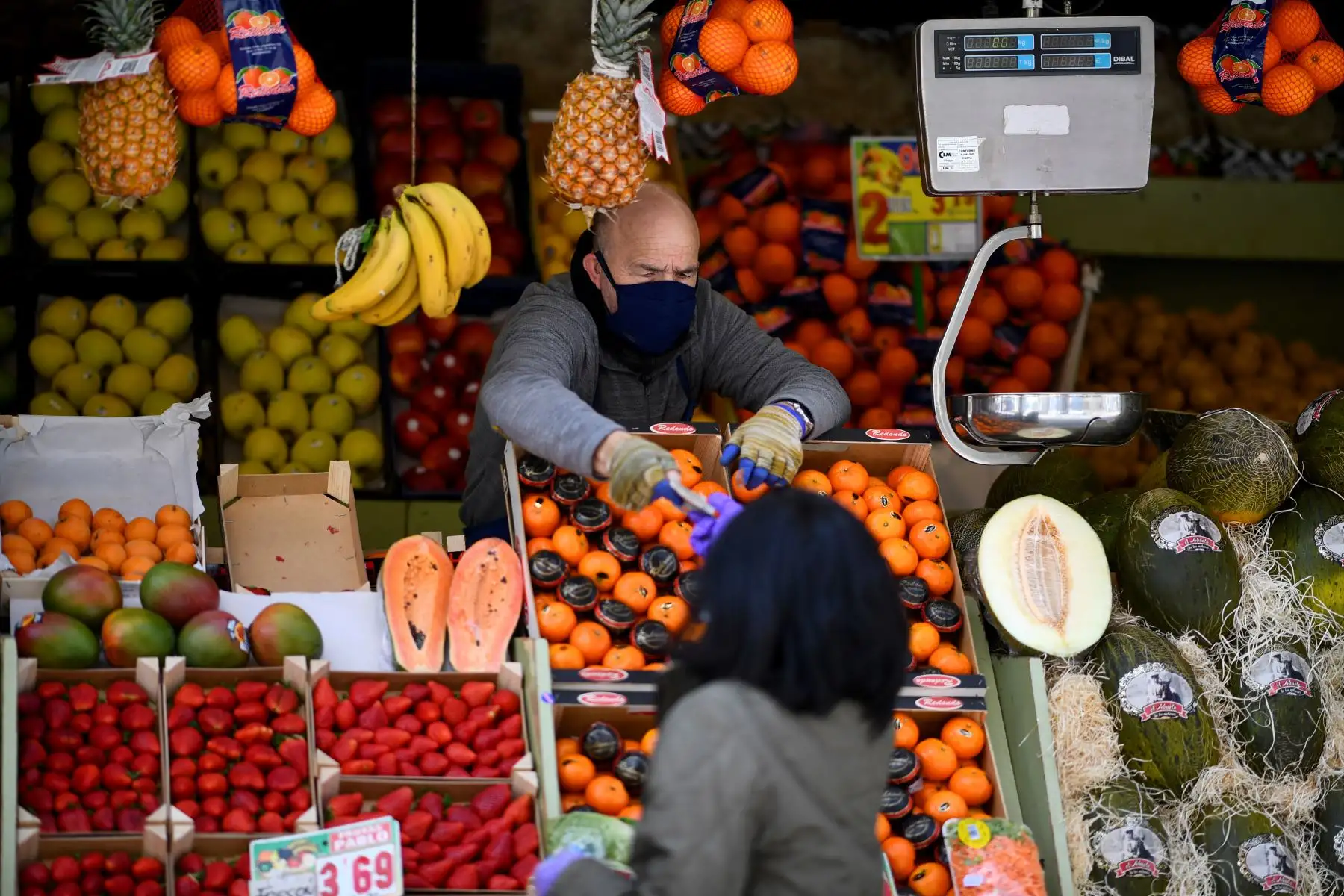 Un hombre con una máscara facial trabaja en una tienda de frutas y verduras en Puente de Vallecas, uno de los distritos más pobres de Madrid. Foto: AFP