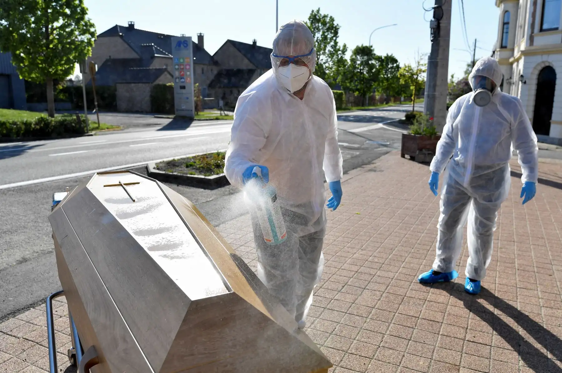 Los empleados de servicios funerarios que usan equipos de protección desinfectan el ataúd de una víctima del COVID-19 frente a la morgue del Hospital Saint-Luc en Namur. Foto: AFP