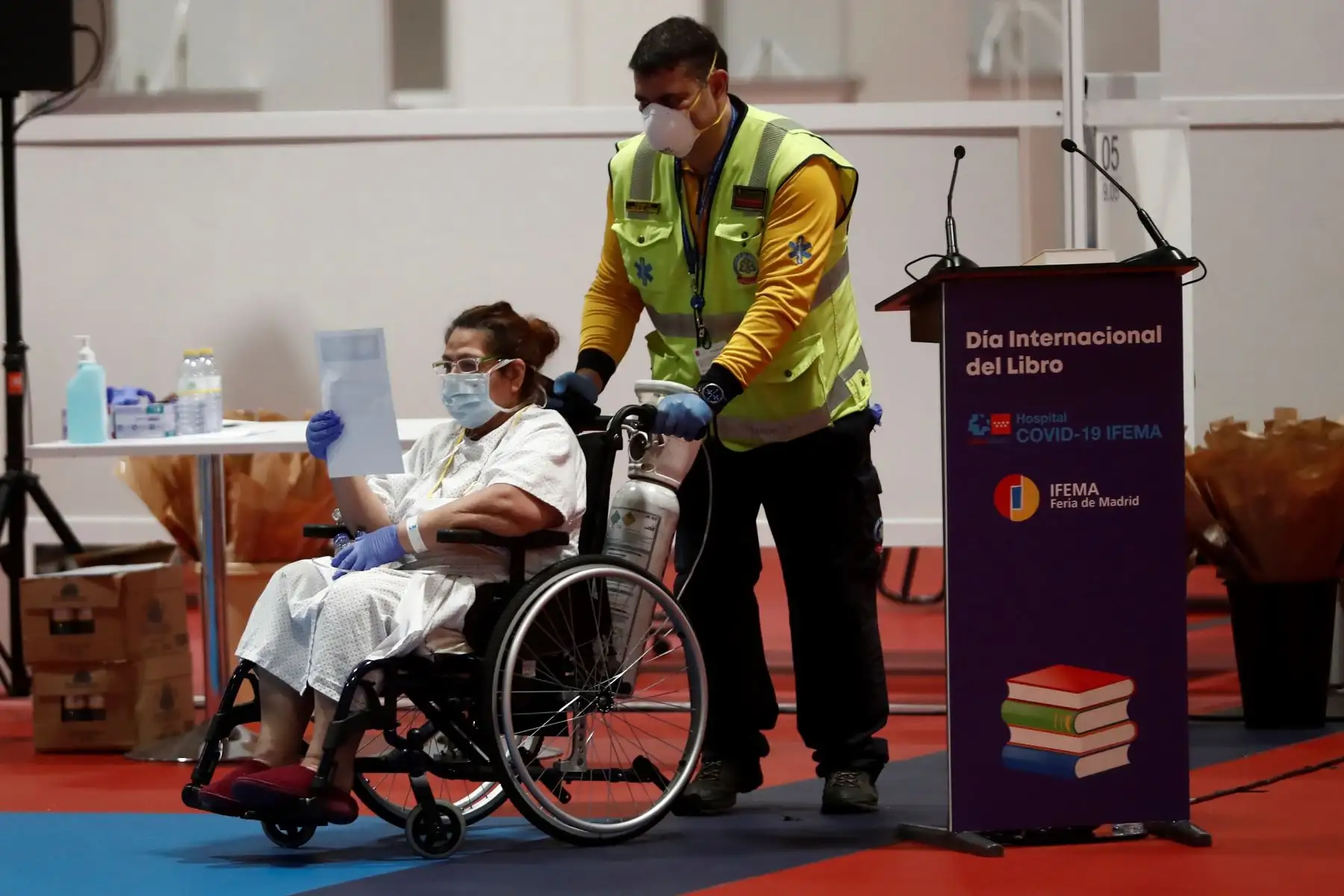 Una paciente en silla de ruedas en el hospital de campaña provisional instalado en Ifema participa en la actividad por el Día del libro, en el que las personas que trabajan allí y los enfermos leen El Quijote y se regalan rosas y claveles.
Foto. EFE