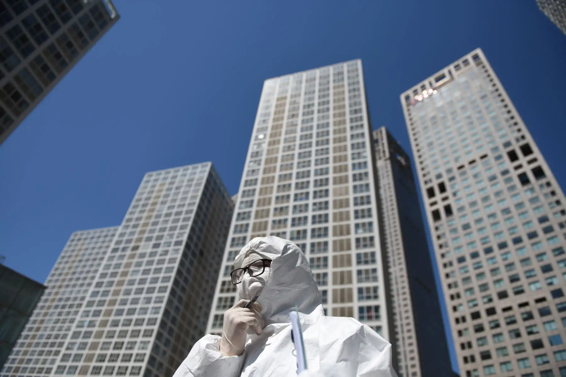 Un trabajador, vestido con un traje protector contra el coronavirus COVID-19, espera para verificar la temperatura de los conductores a la entrada del estacionamiento de un complejo comercial en Beijing el 22 de abril de 2020. Foto: AFP