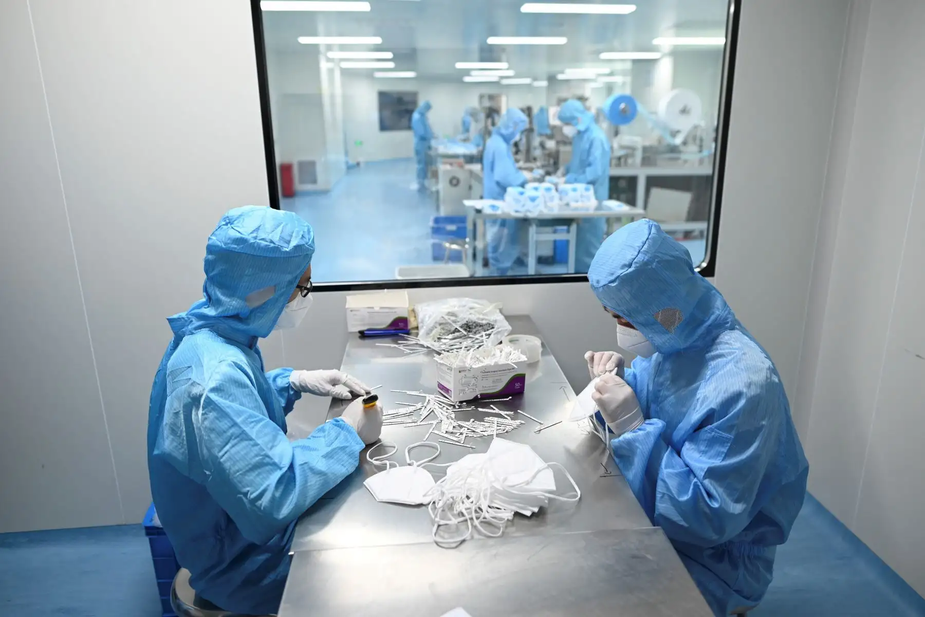 Dos trabajadores con trajes protectores fabrican máscaras en Naton Medical Group, una compañía que fabrica equipos médicos en Beijing. Foto: AFP