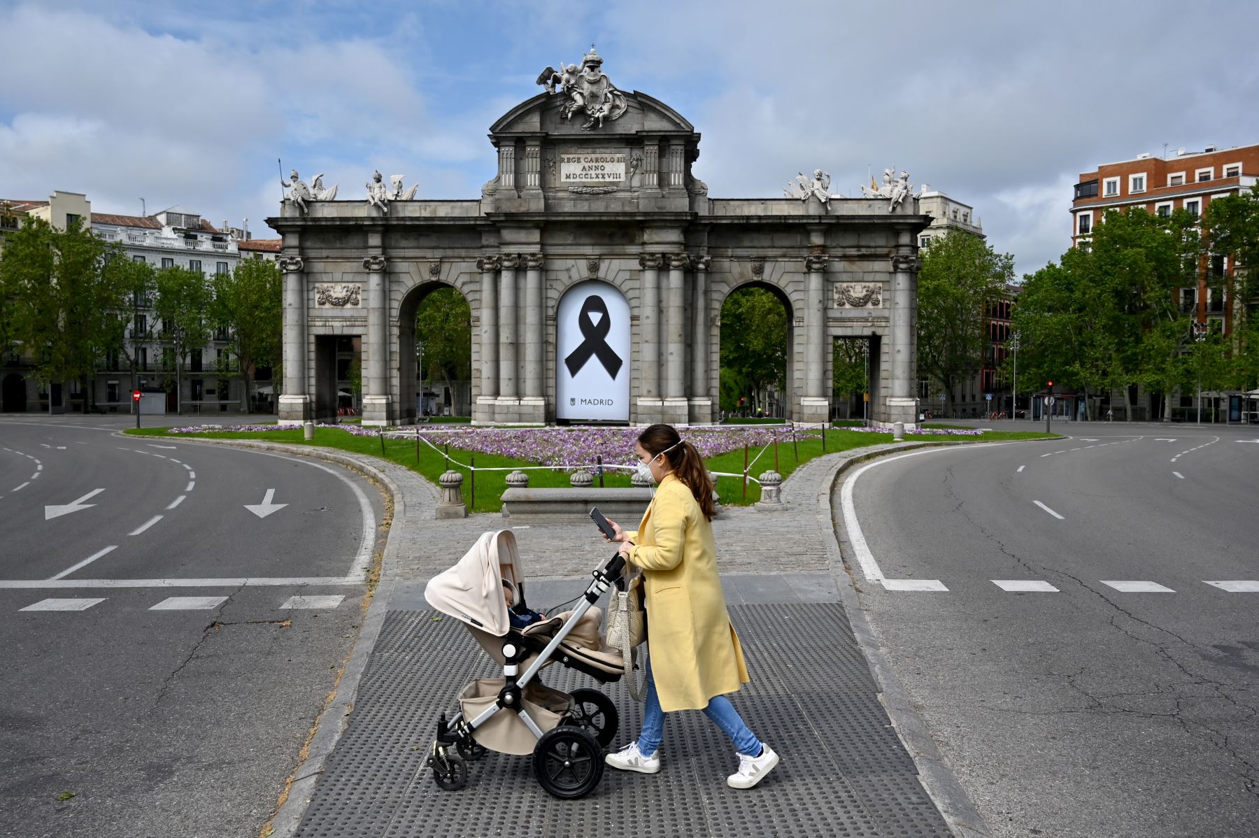 Una mujer empuja una carriola frente al monumento de la Puerta de Alcalá, en Madrid, durante un cierre nacional para prevenir la propagación del coronavirus. Foto: AFP.