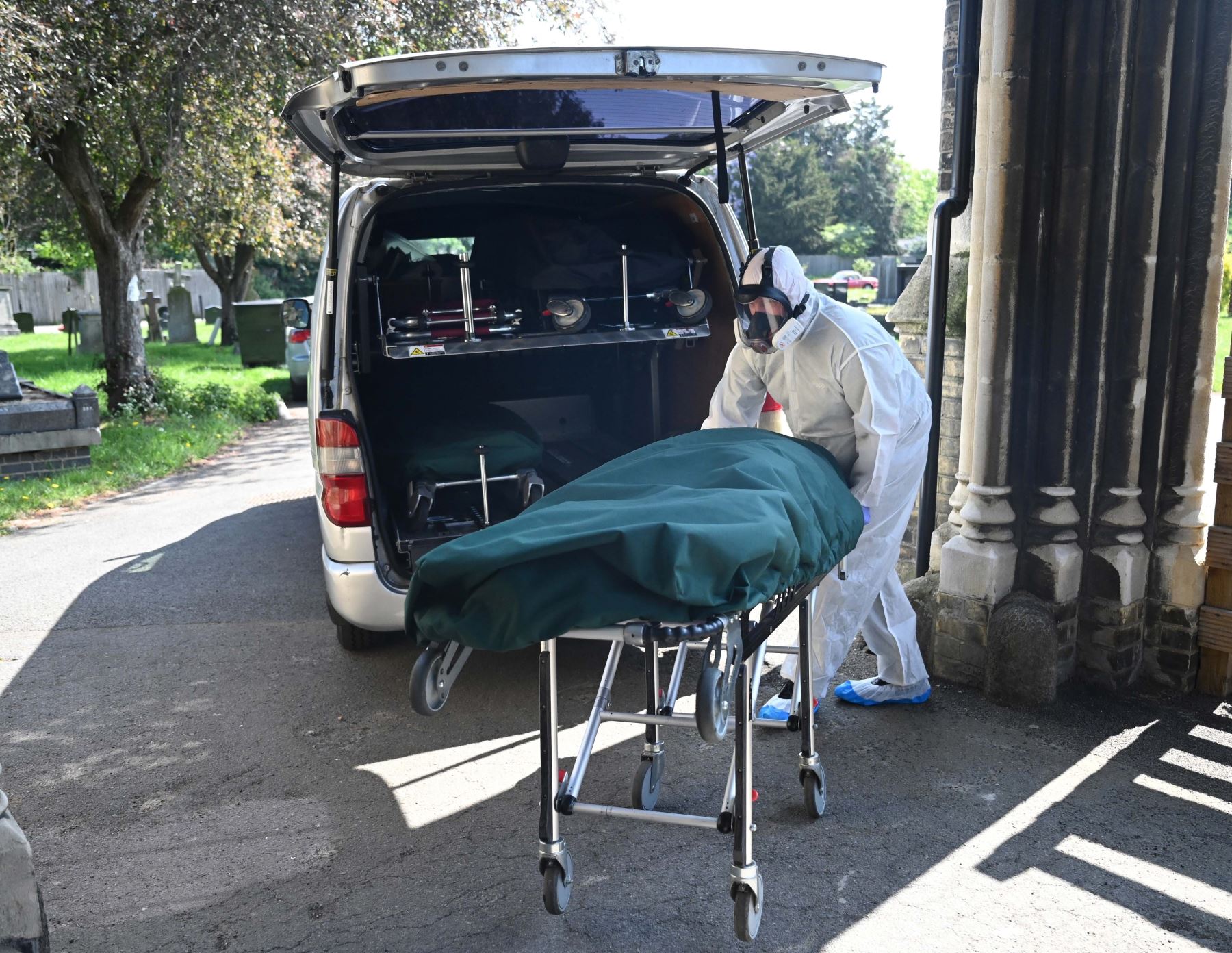El trabajador de una funeraria usa traje protector para mover un cuerpo de una persona, que murió de coronavirus. Foto: EFE