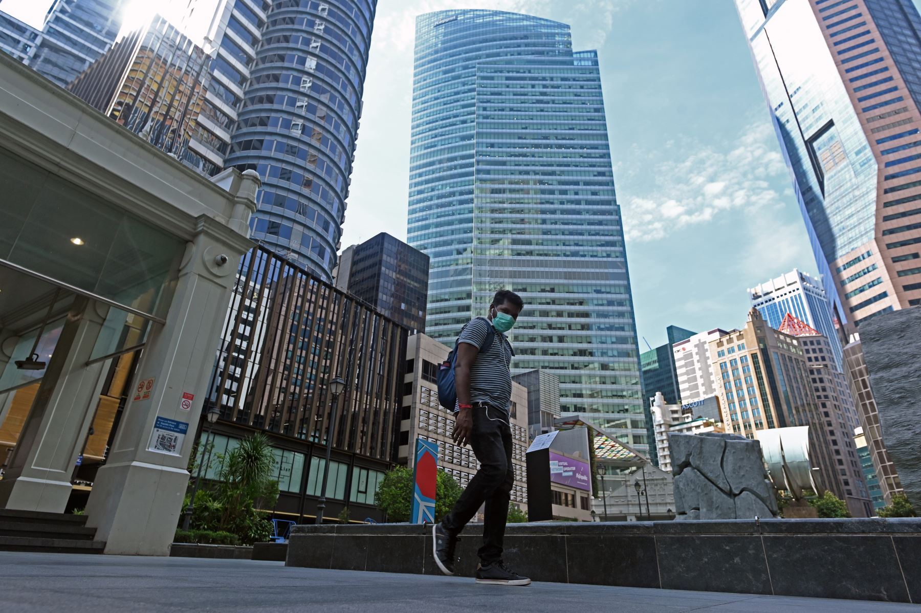 Un hombre que usa una mascarilla como medida preventiva contra la propagación del coronavirus COVID-19 camina junto a edificios comerciales en el distrito financiero financiero de Raffles Place en Singapur. Foto: AFP