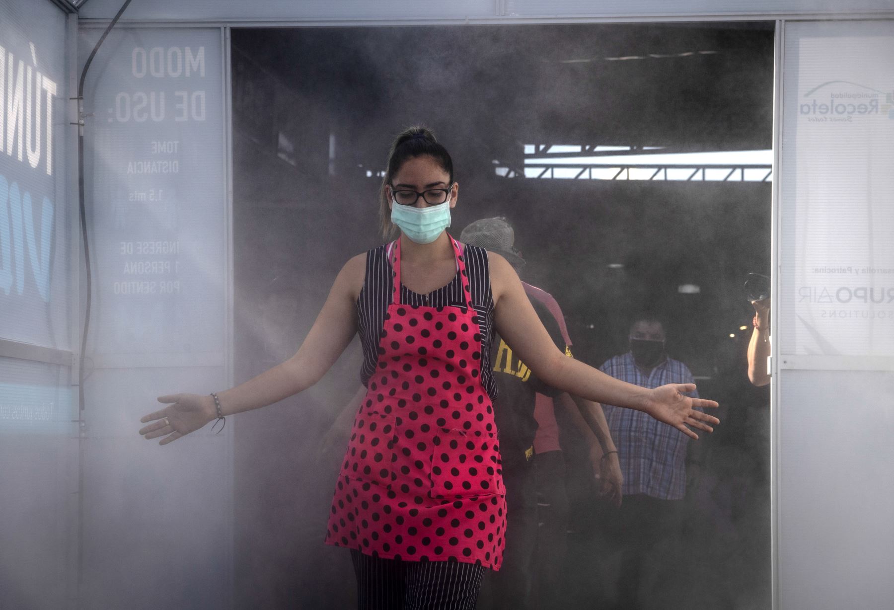 Una mujer usa una máscara facial mientras atraviesa un túnel de limpieza y desinfección llamado "Túnel de la Vida", que a través del agua electrolizada (ácido hipocloroso) ayuda a desinfectar a las personas que ingresan al mercado central de Santiago. Foto: AFP
