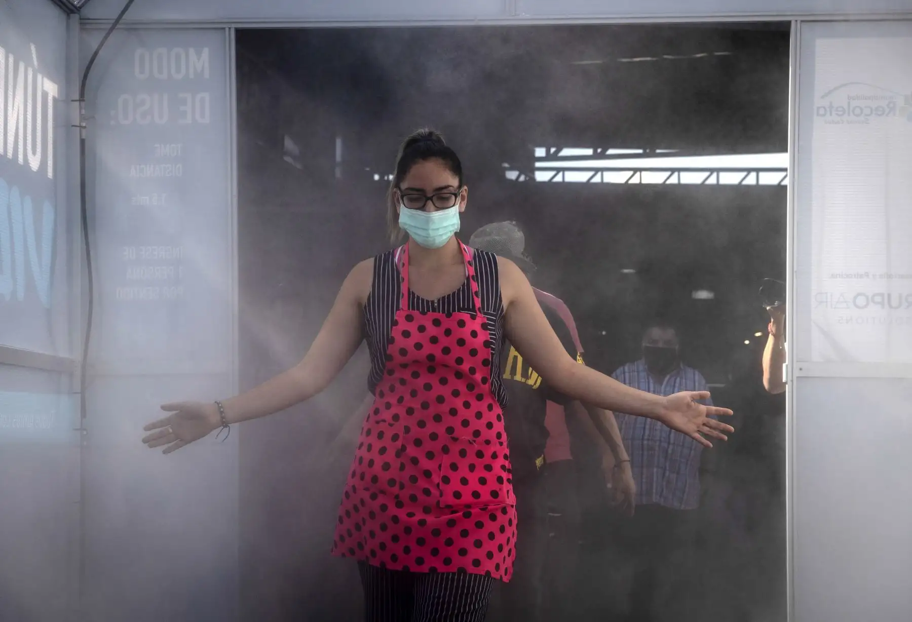 Una mujer usa una máscara facial mientras atraviesa un túnel de limpieza y desinfección llamado "Túnel de la Vida", que a través del agua electrolizada (ácido hipocloroso) ayuda a desinfectar a las personas que ingresan al mercado central de Santiago. Foto: AFP