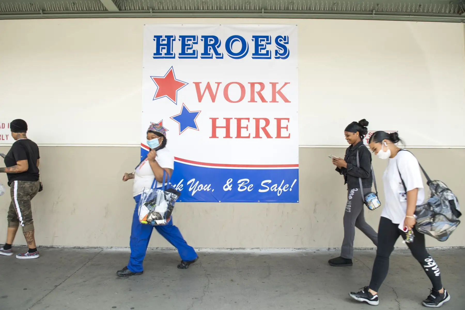 Los empleados caminan junto a un letrero que dice "Los héroes trabajan aquí" fuera de una planta de producción en Los Ángeles. Foto: AFP