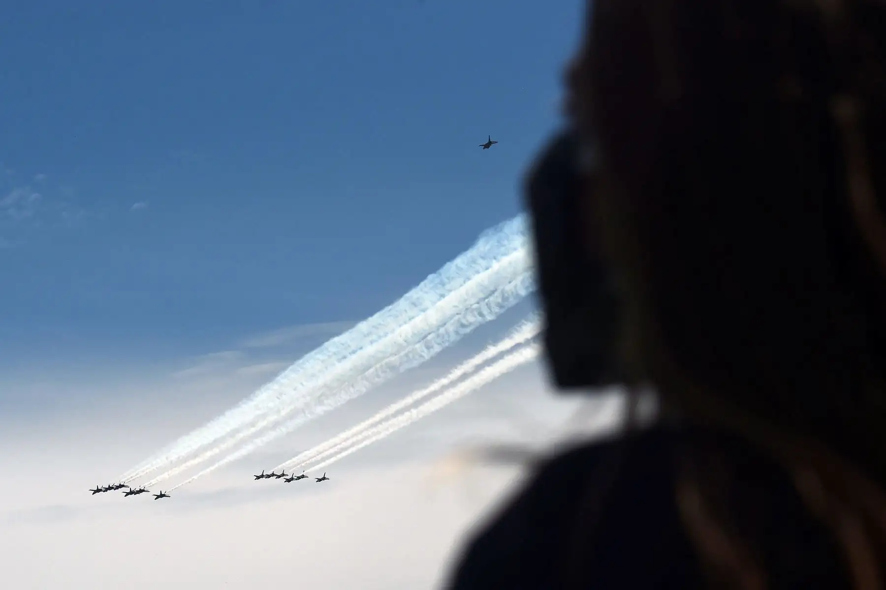 Una persona que usa una máscara facial observa cómo los Blue Angels de la Marina y  los Thunderbirds de la Fuerza Aérea de EE. UU. vuelvan sobre Arlington, Virginia. Foto: AFP