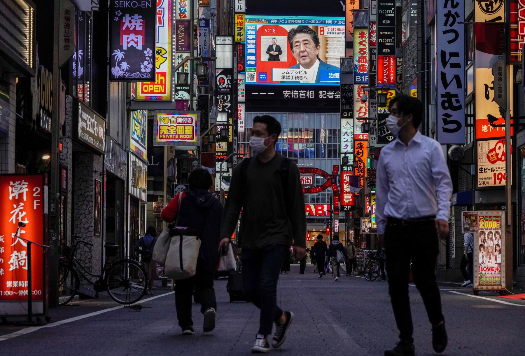 Los peatones pasan frente a una pantalla de televisión pública que muestra al primer ministro japonés Shinzo Abe hablando en una conferencia de prensa televisada en Kabukicho, el distrito de entretenimiento más grande y popular de Shinjuku en Tokio, Japón. Foto: EFE
