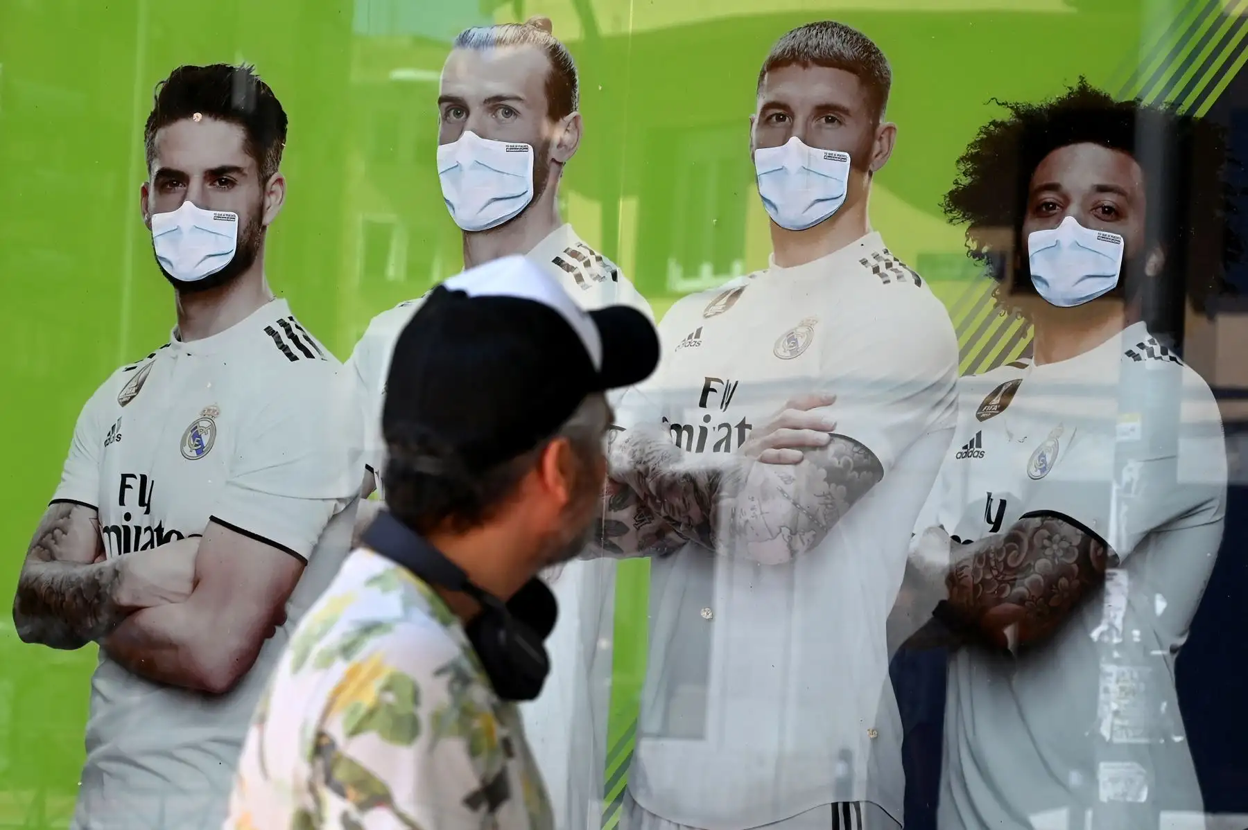 Un hombre mira el cartel publicitario de una sala de juego que representa a Isco, Gareth Bale, Sergio Ramos y Marcelo con máscaras faciales, en Madrid. Foto: AFP