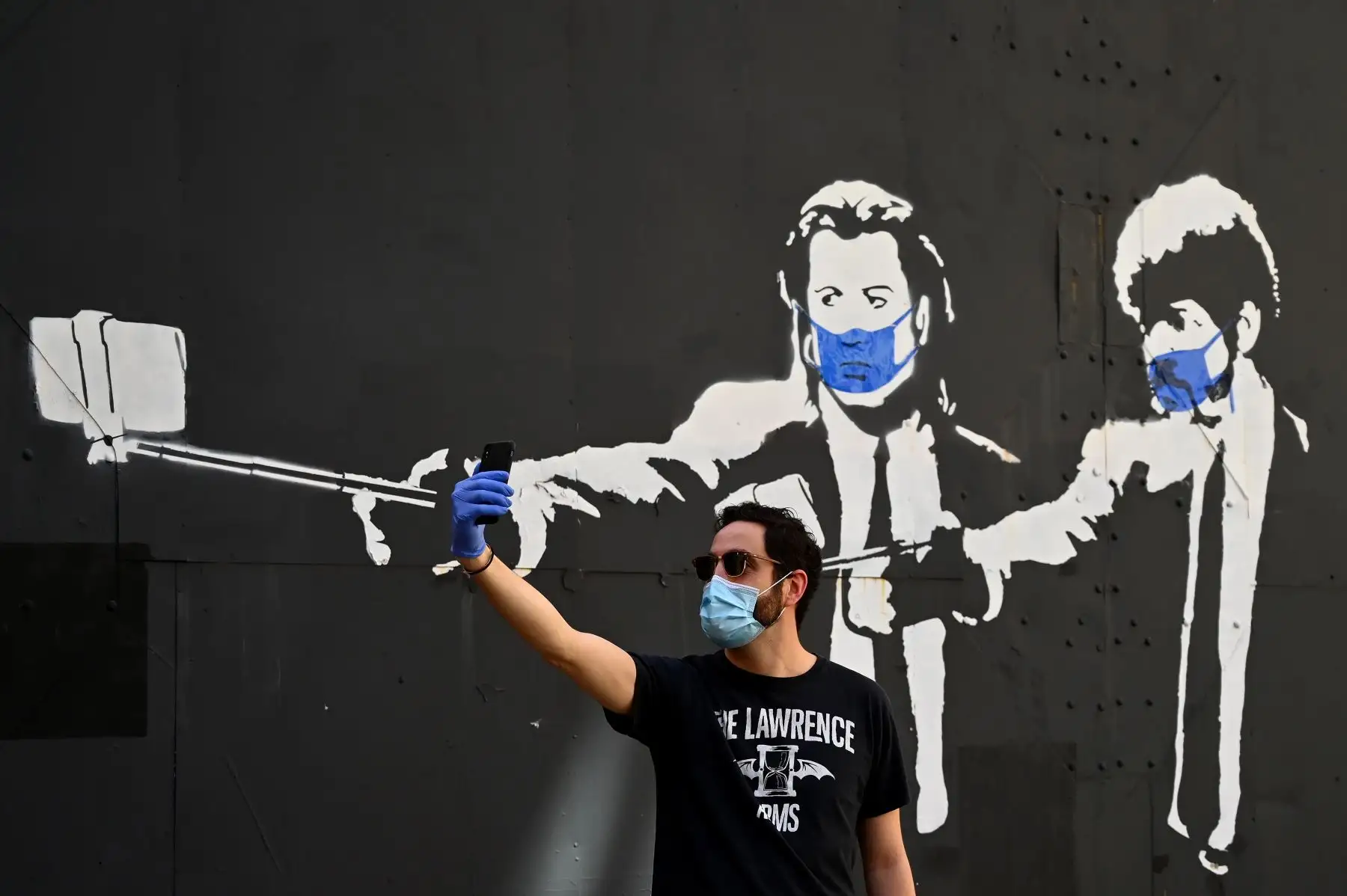 Un hombre se toma una foto selfie frente a una plantilla de graffiti que representa a los actores estadounidenses John Travolta y Samuel L. Jackson. Foto: AFP