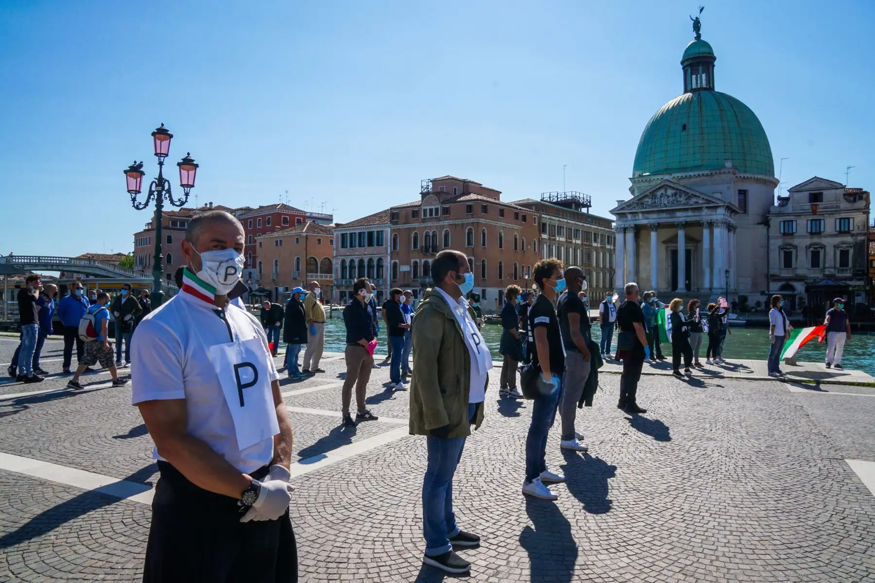 Los comerciantes que solicitan la reapertura de las tiendas y las actividades comerciales se reúnen para una protesta flashmob fuera de la estación de tren de Santa Lucía en el Gran Canal el 4 de mayo de 2020 en Venecia. Foto: AFP