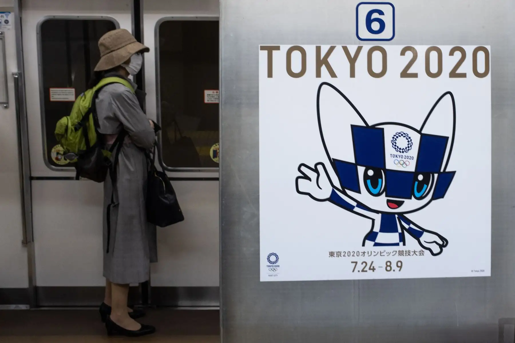Una pasajera con una máscara facial se encuentra al lado de un cartel que muestra a la mascota olímpica de Tokio 2020, Miraitowa, en un tren en Tokio. Foto: AFP