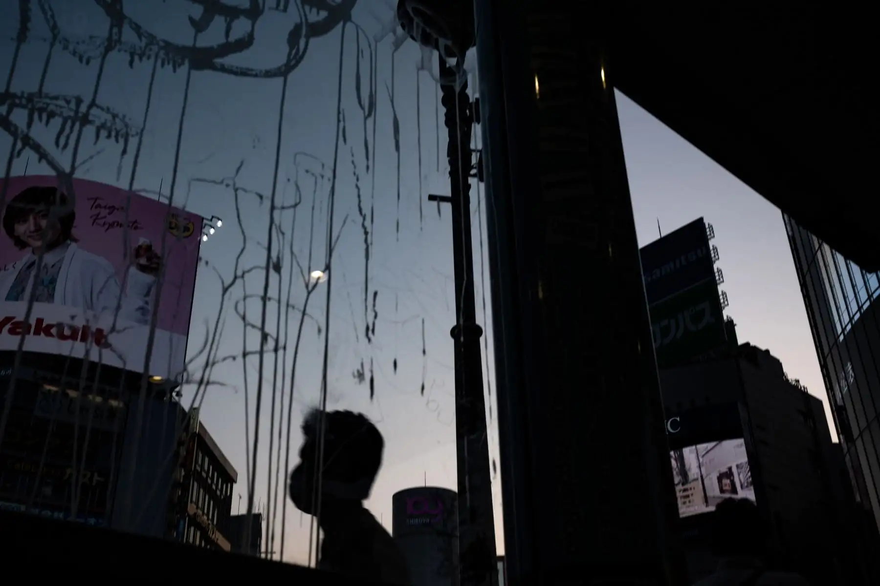 Un peatón se refleja en las ventanas de un edificio al atardecer en una calle en el distrito de Shibuya. Foto: AFP