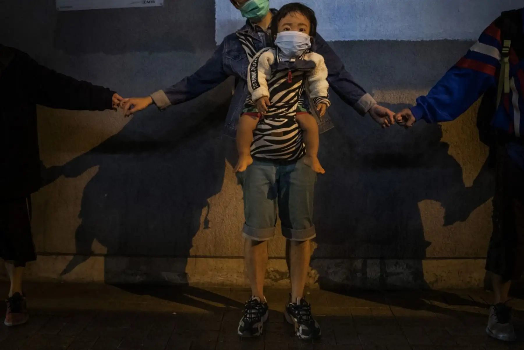 Un niño se sienta en un portador con una máscara mientras los manifestantes antigubernamentales se toman de la mano para formar una cadena humana en señal de solidaridad en la bahía de Kowloon, Hong Kong, China. Foto: Reuters/Pulitzer