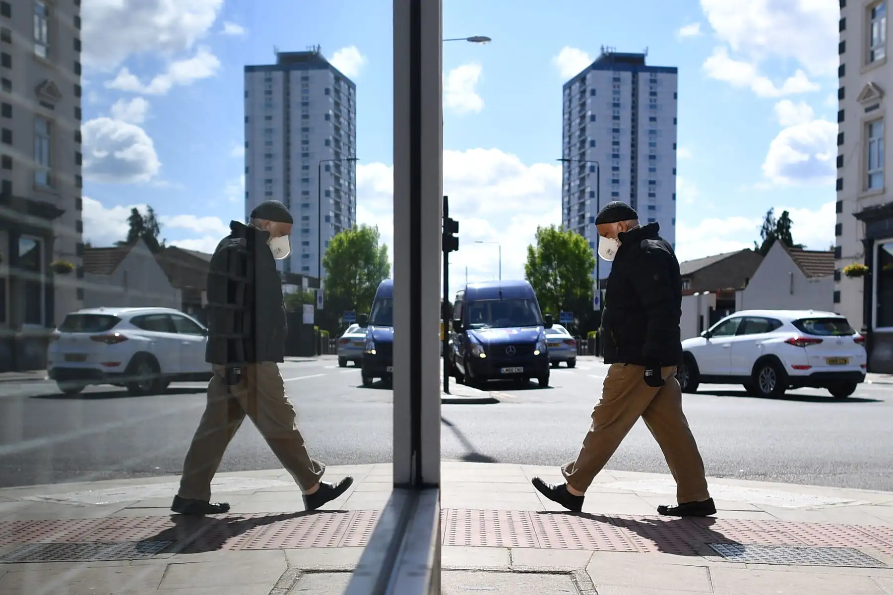 Un peatón con una máscara facial se refleja en la ventana de una tienda cerrada en el distrito londinense de Newham. Foto: AFP