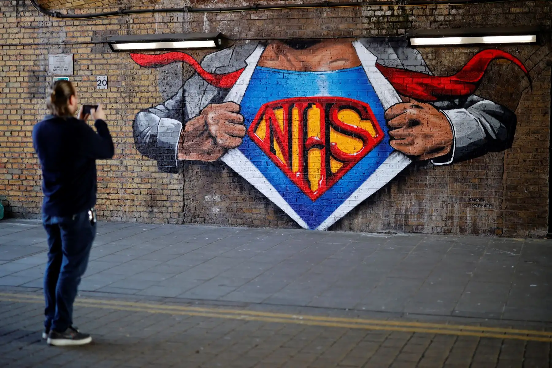 Un peatón toma una fotografía de una obra de arte que celebra el Servicio Nacional de Salud (NHS) pintada en una pared de ladrillos en el centro de Londres. Foto: AFP