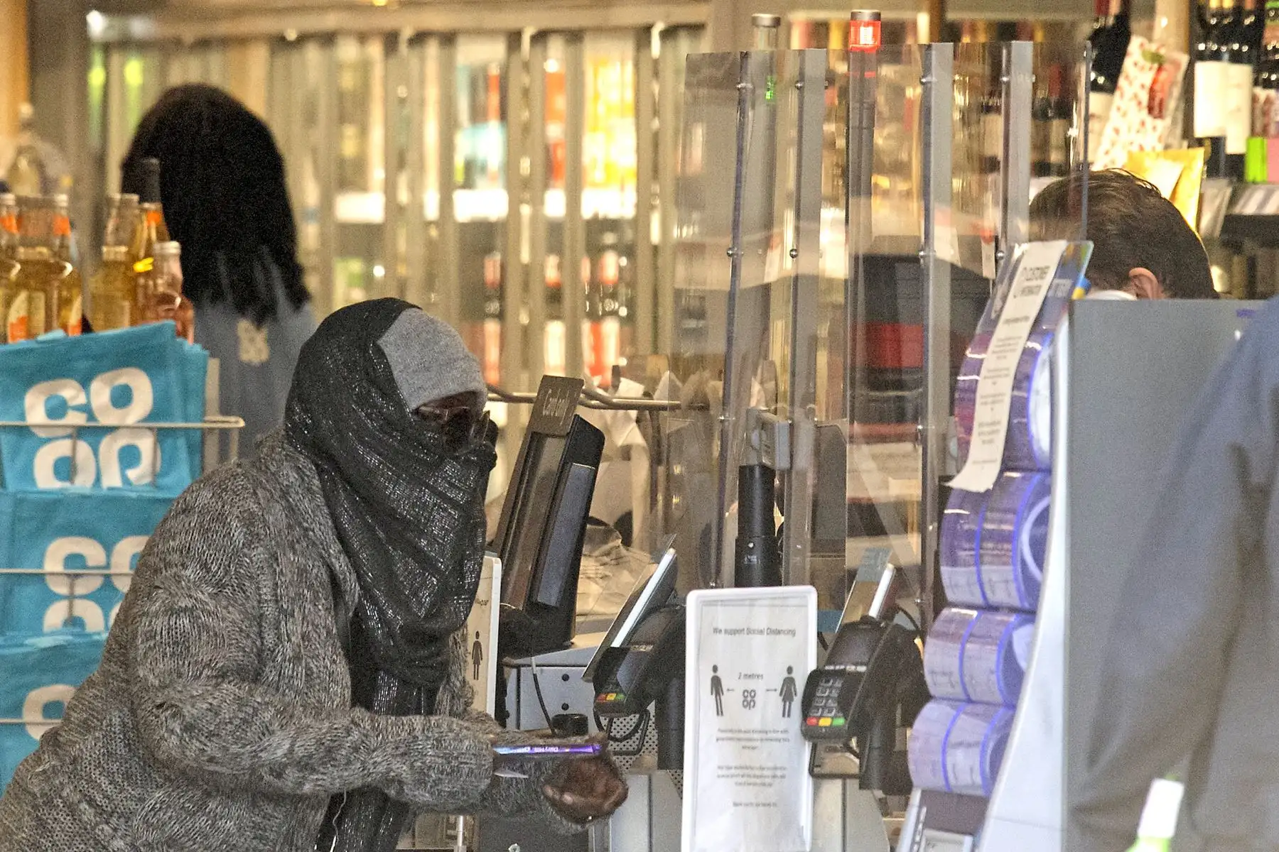 Un cliente en una tienda Co-Op se encuentra frente a unalamina protectora de perspex en Balham, sur de Londres mientras la vida en Gran Bretaña continúa durante el cierre nacional debido al nuevo coronavirus. Foto: AFP