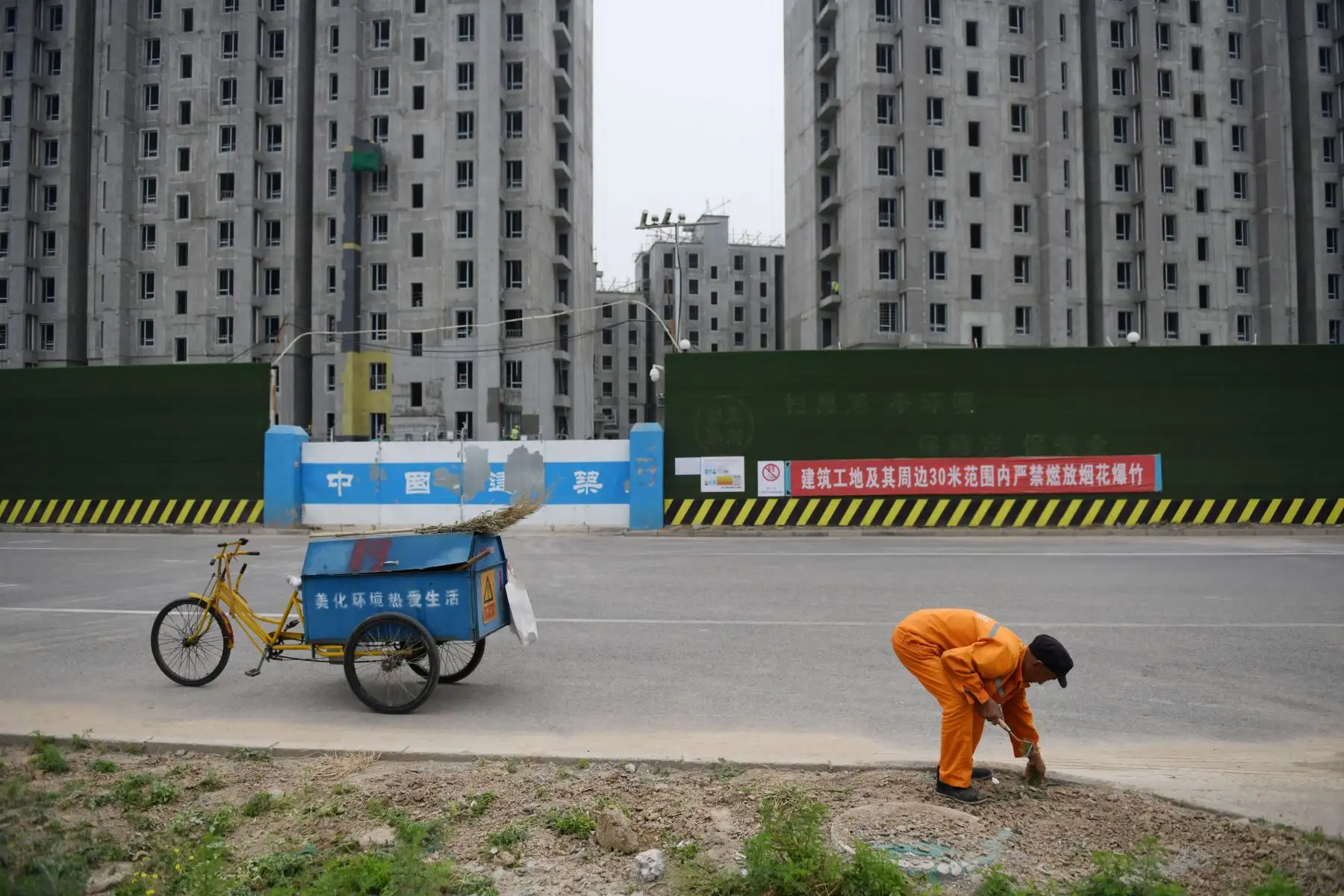 Un trabajador limpia las malezas fuera del sitio de construcción de un complejo residencial en las afueras de Beijing. Foto: AFP