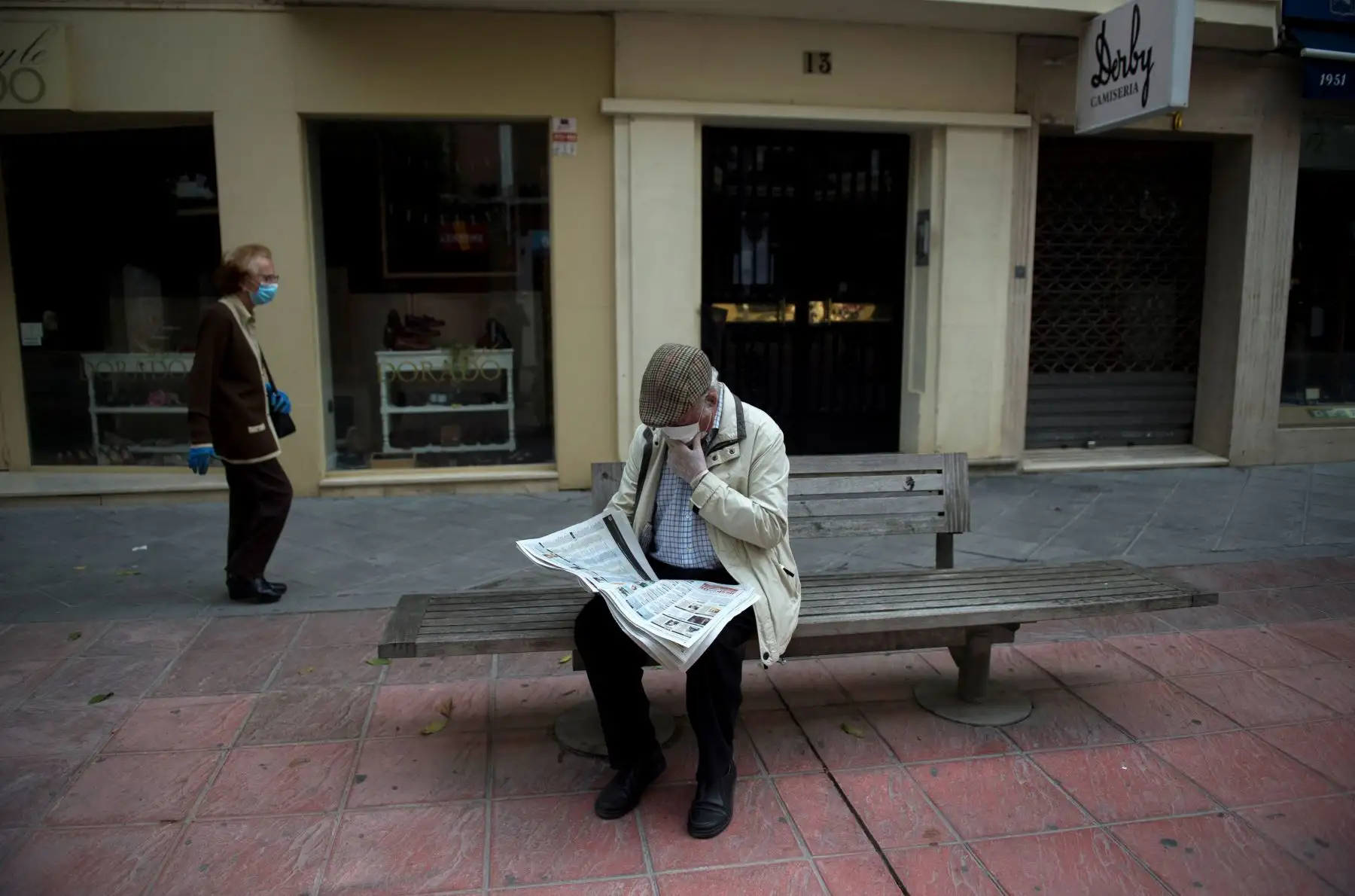 Un hombre lee el periódico sentado en un banco de una calle en Sevilla. Foto: AFP