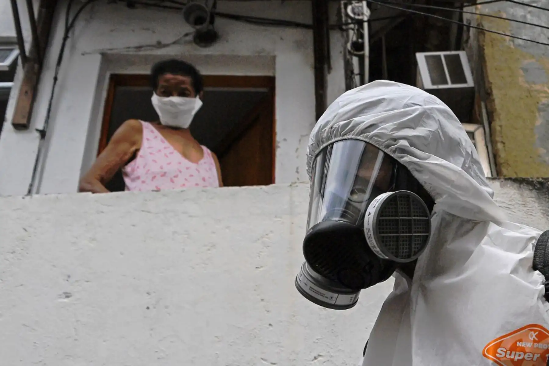Una mujer mira desde la puerta de su casa mientras un voluntario desinfecta una calle de la favela de Babilonia, en Río de Janeiro. Foto: AFP