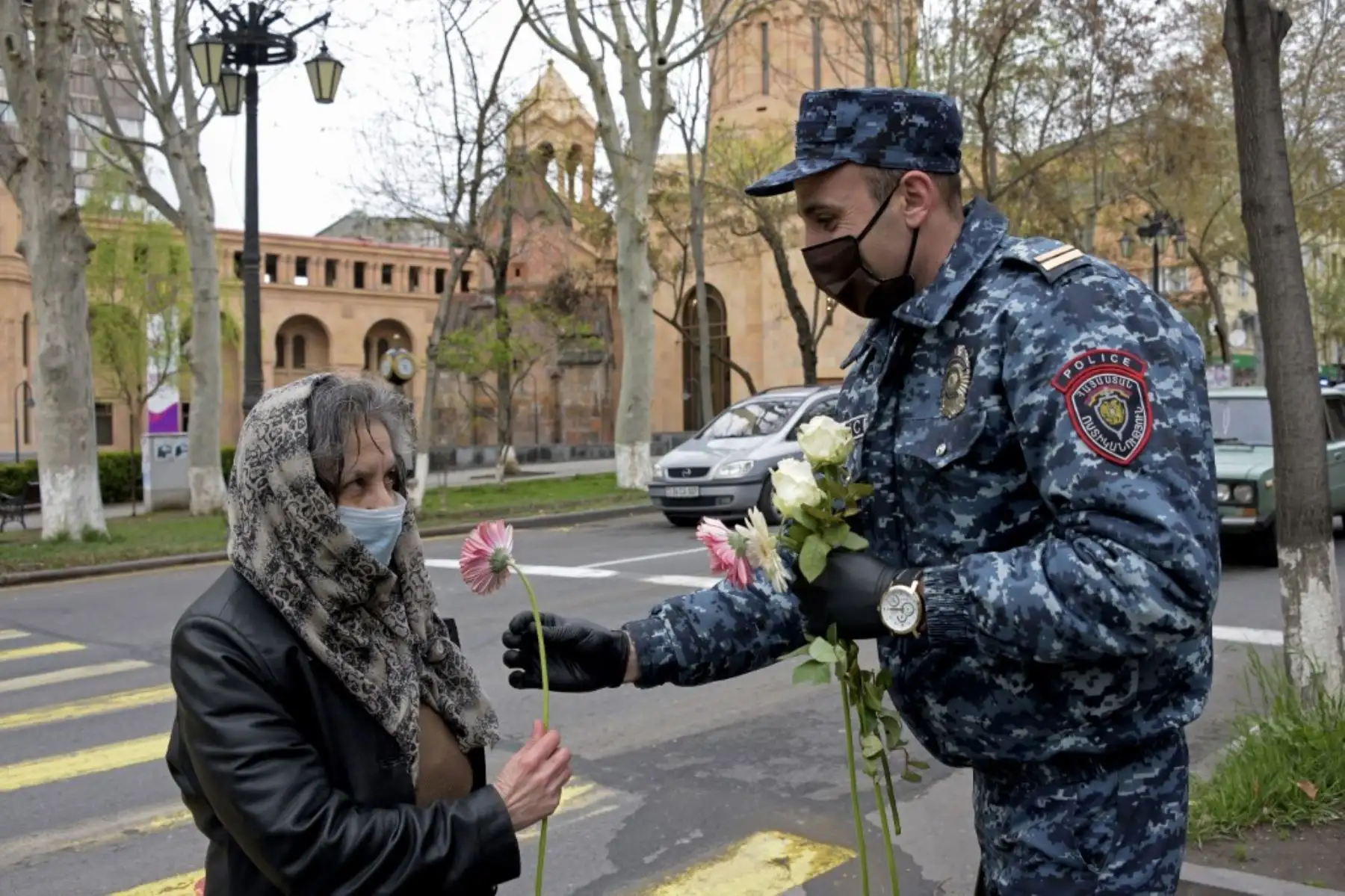 Un oficial de policía con una máscara facial y guantes entrega una flor a una mujer por el Día de la Madre en el centro de la ciudad de Ereván. Foto: AFP