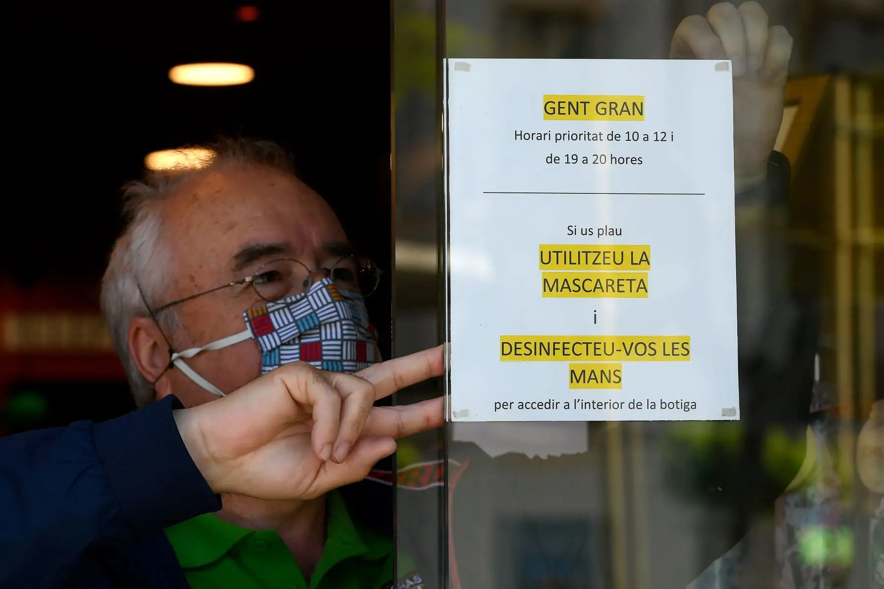 Un hombre pega un letrero pidiéndole a las personas que usen mascarillas y se desinfecten las manos antes de ir a una tienda en Tarragona. Foto: AFP