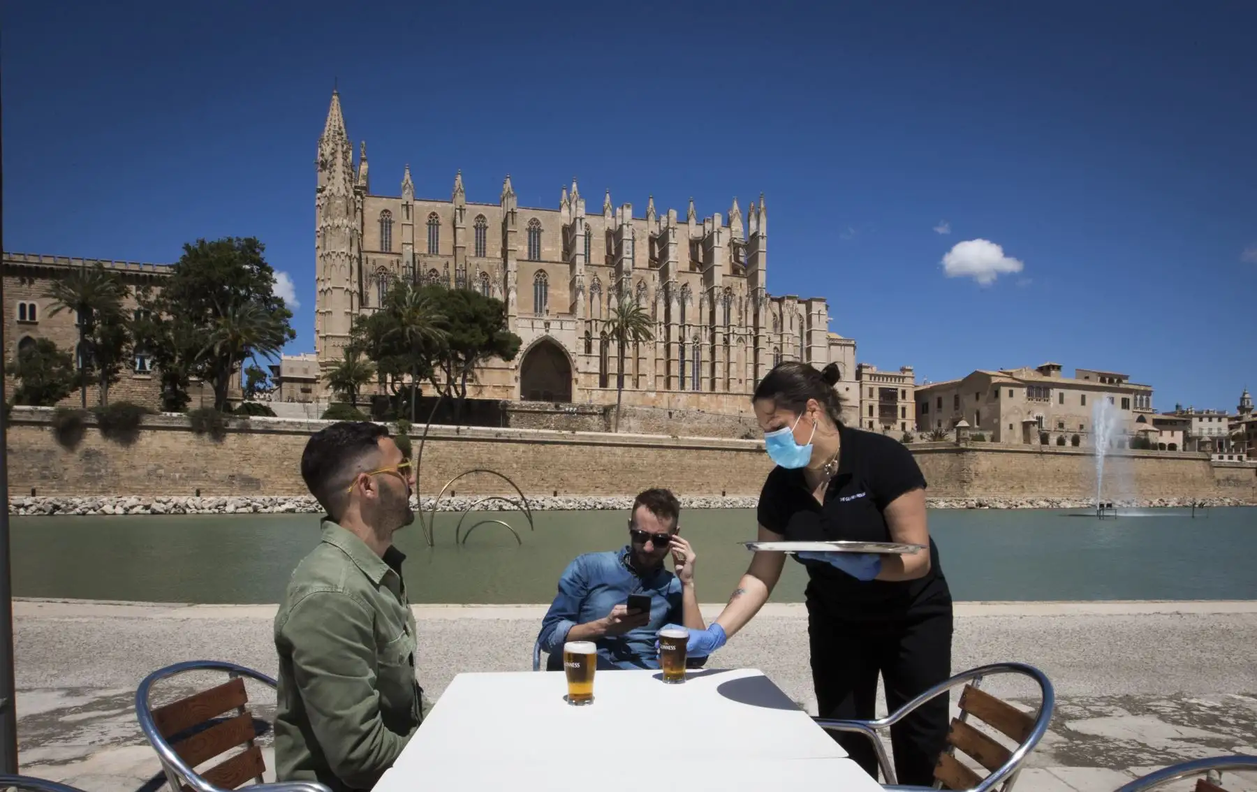 Una camarera con una máscara facial y guantes sirve a los clientes en un bar con terraza cerca de la Catedral de Palma de Mallorca el 11 de mayo de 2020, mientras España avanzaba hacia la reducción de su estricto encierro en ciertas regiones. Foto: AFP