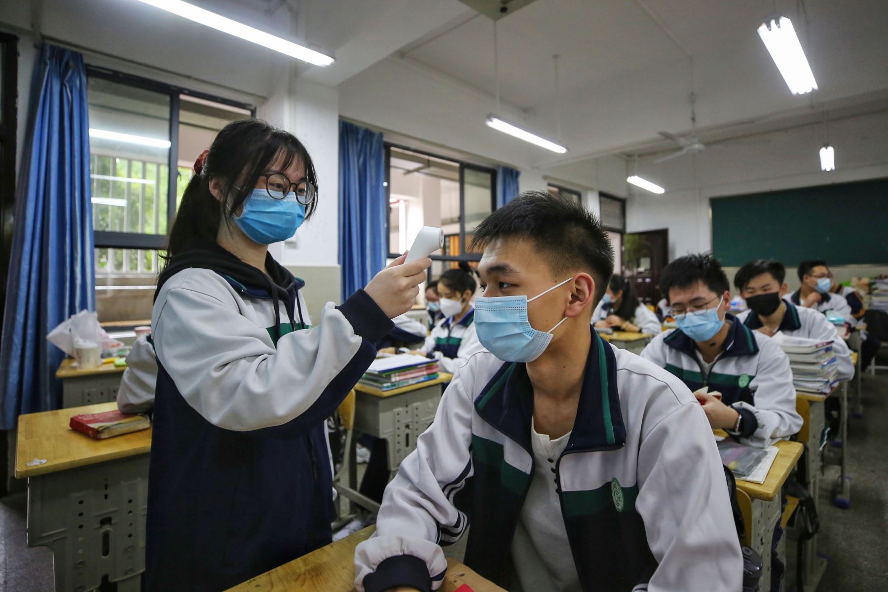 Una estudiante de secundaria verifica la temperatura corporal de sus compañeros de aula antes de una clase en Wuhan, provincia central de Hubei, China. Foto: AFP.