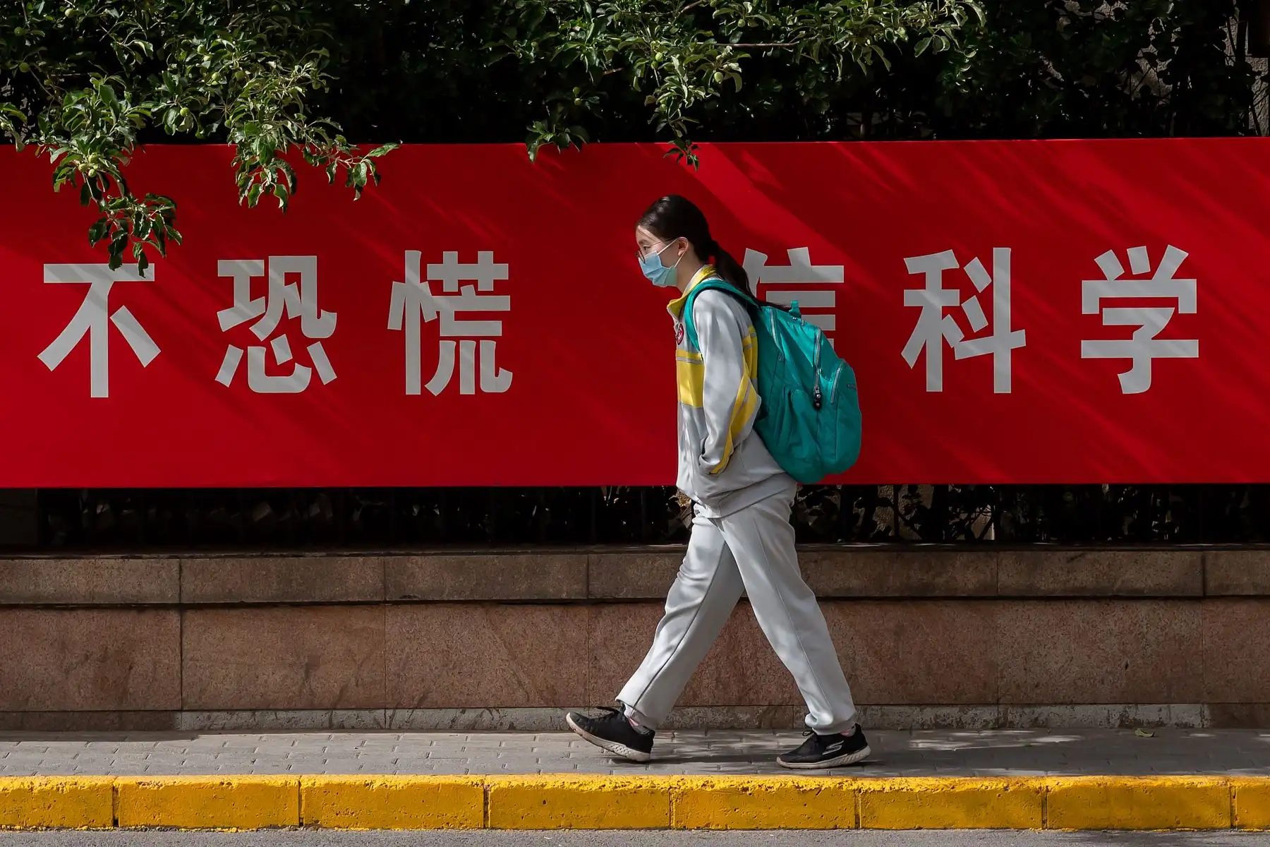 Una estudiante con una máscara facial en medio de preocupaciones por el coronavirus COVID-19 pasa junto a un cartel de propaganda en una calle que dice "No Panic Trust Science" cuando sale de una escuela secundaria en Beijing el 11 de mayo de 2020. Foto: AFP