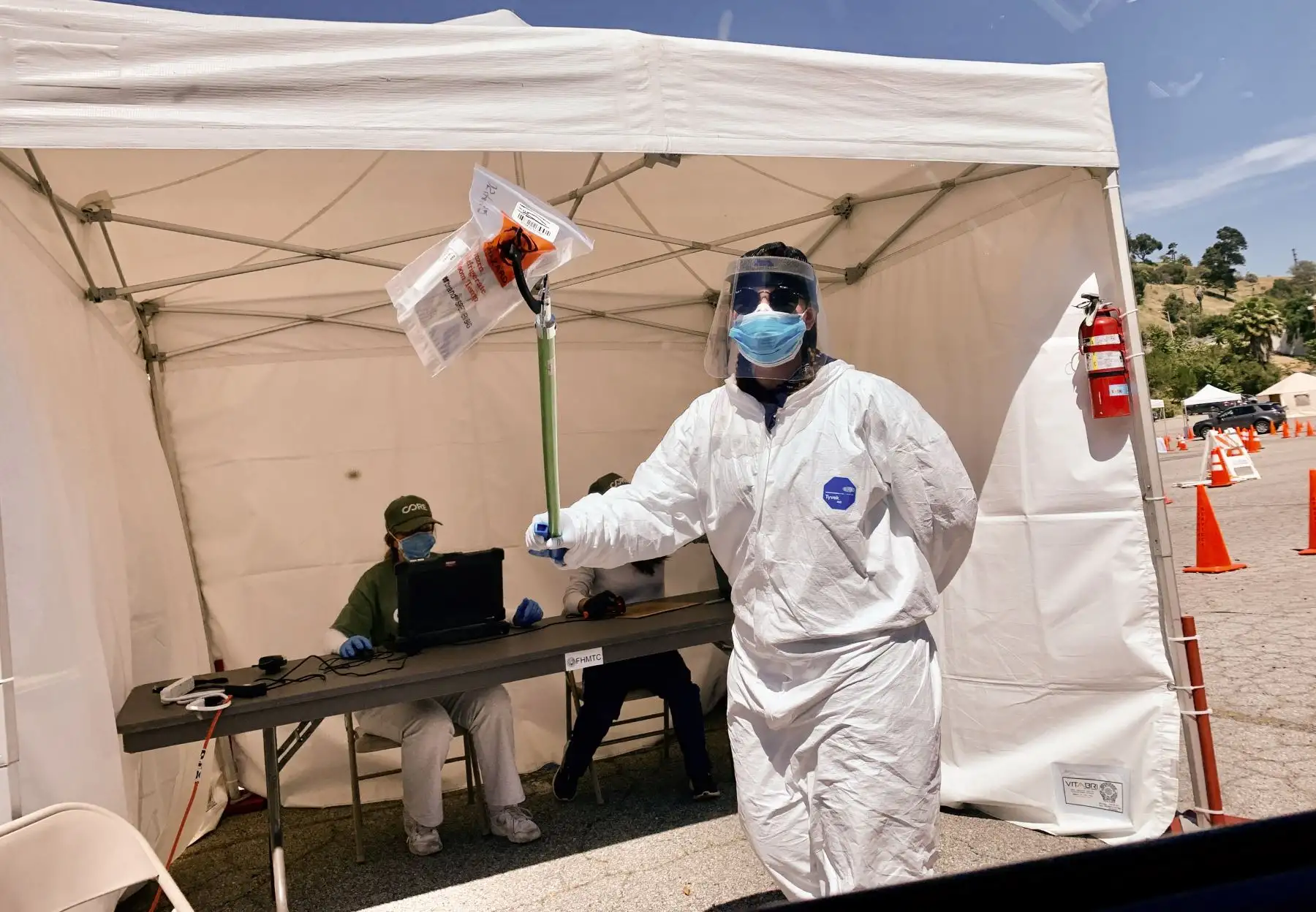 El personal de un centro de pruebas COVID-19 utiliza una herramienta de extensión para pasar un kit de prueba autoadministrado con un hisopo bucal a un conductor en un centro de pruebas de detección de la nueva enfermedad por coronavirus. Foto: AFP