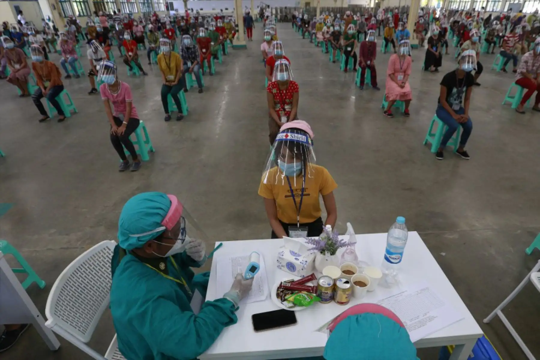 Un trabajador de salud militar que usa equipo de protección toma la temperatura corporal de un trabajador en la zona industrial de Hlaing Thar Yar en un esfuerzo por contener la propagación del COVID-19 coronavirus en Yangon. Foto: AFP