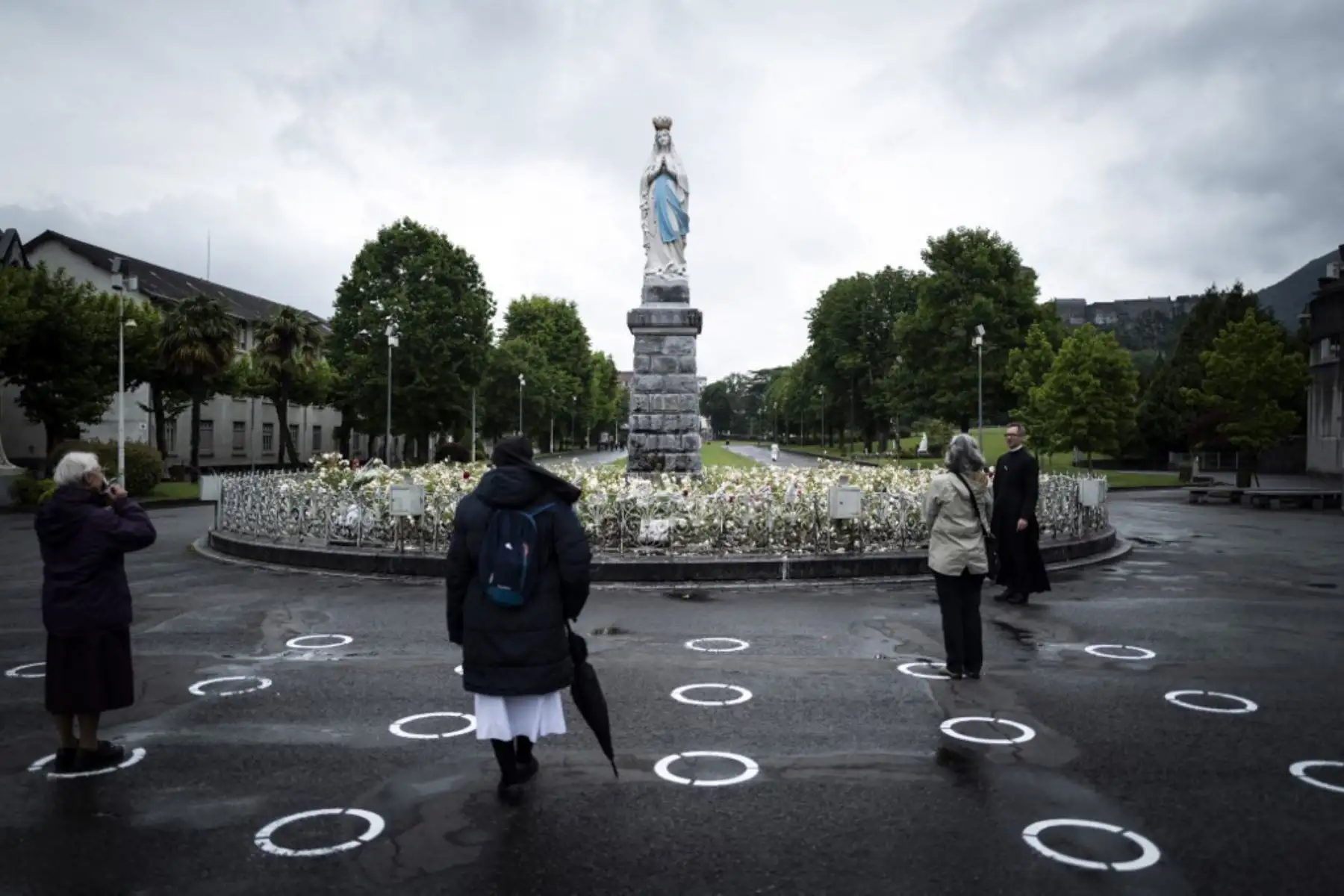 Peregrinos se paran en carteles de distanciamiento social frente a la estatua de La Virgen coronada en el Santuario de Nuestra Señora de Lourdes en Francia. Foto: AFP